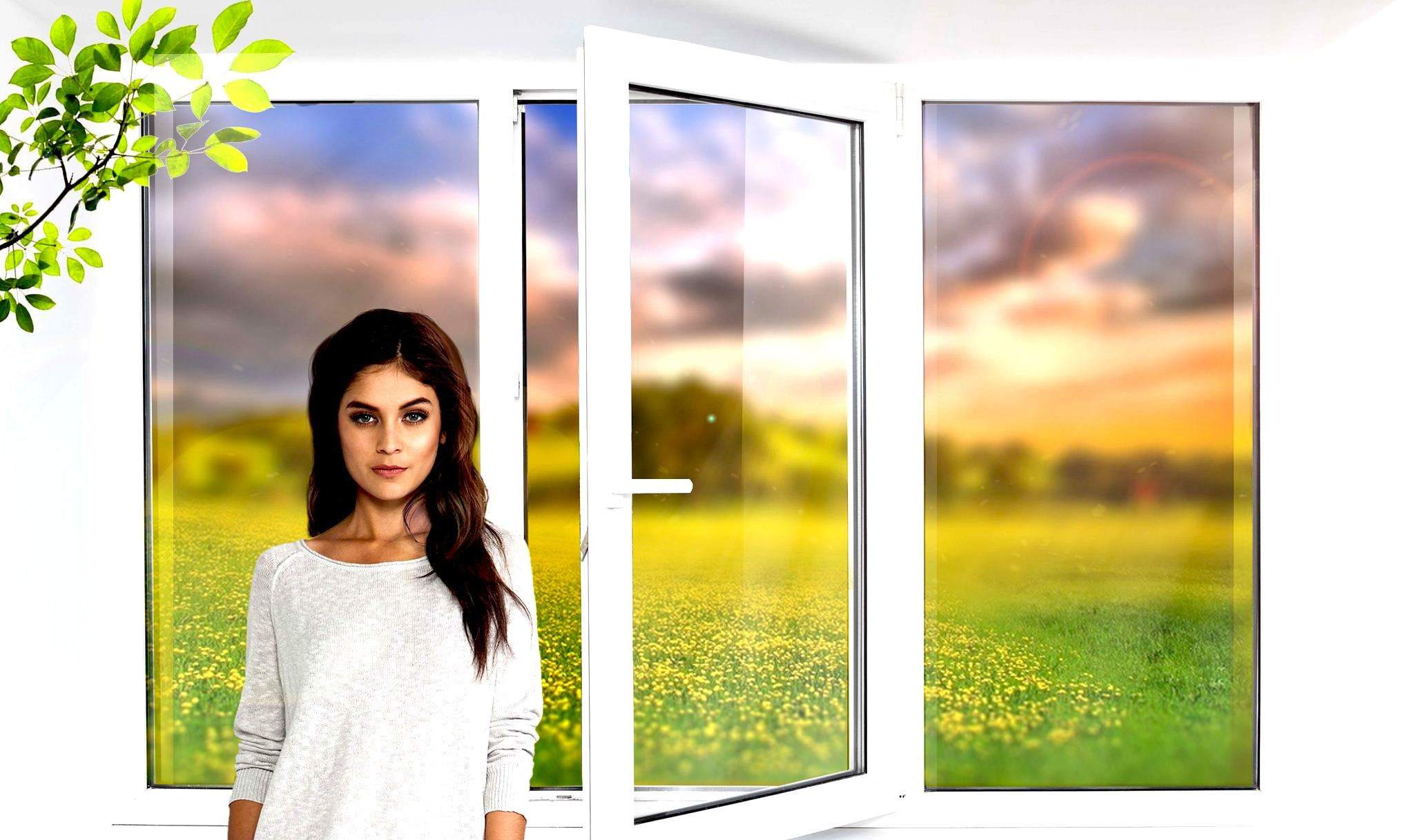 Темноволосая девушка в белом платье стоит у раскрытого пластикового окна с видом на летний луг.