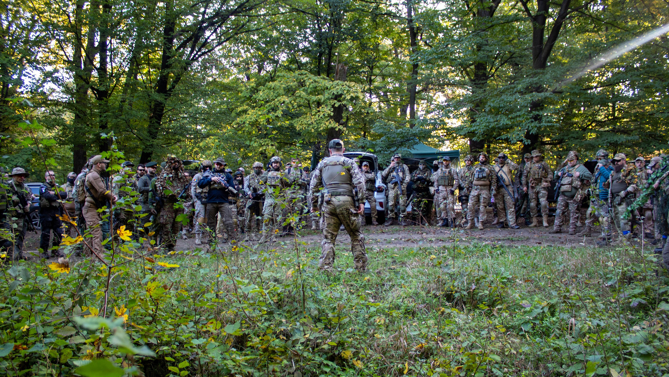Airsoft team in camouflage gear preparing for a competition in a dense forest.