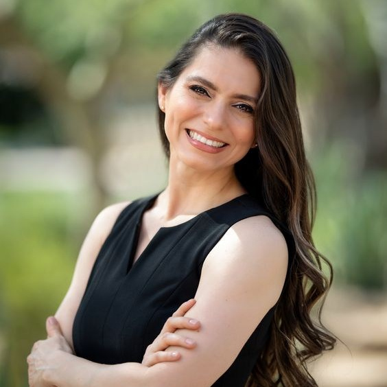 Smiling woman in a black sleeveless dress standing outdoors with arms crossed