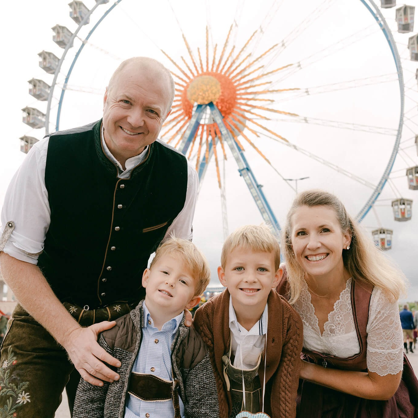 Familie in bayerischer Tracht vor dem Oktoberfest-Riesenrad auf der Theresienwiese in München, Deutschland