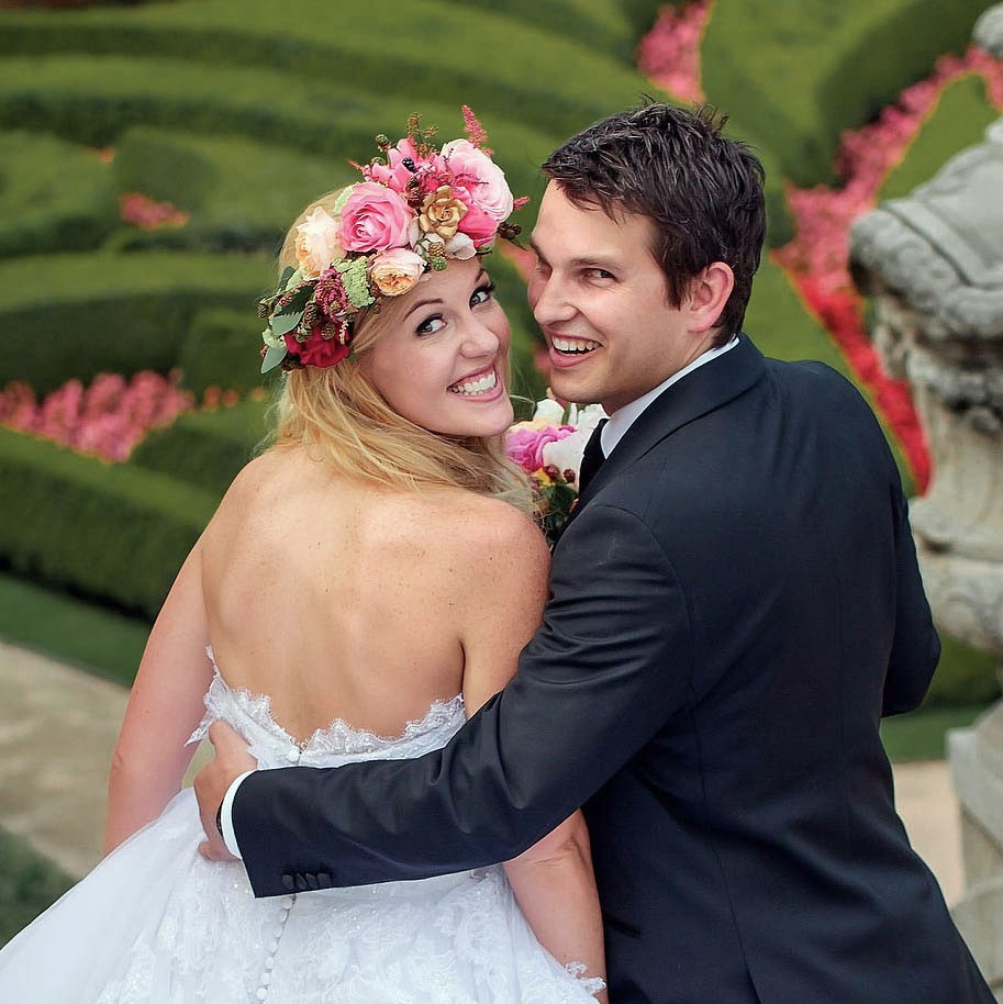 Smiling blonde-haired Swiss bride smiles lovingly towards her Italian groom as he looks towards the camera at a garden in Prague. 