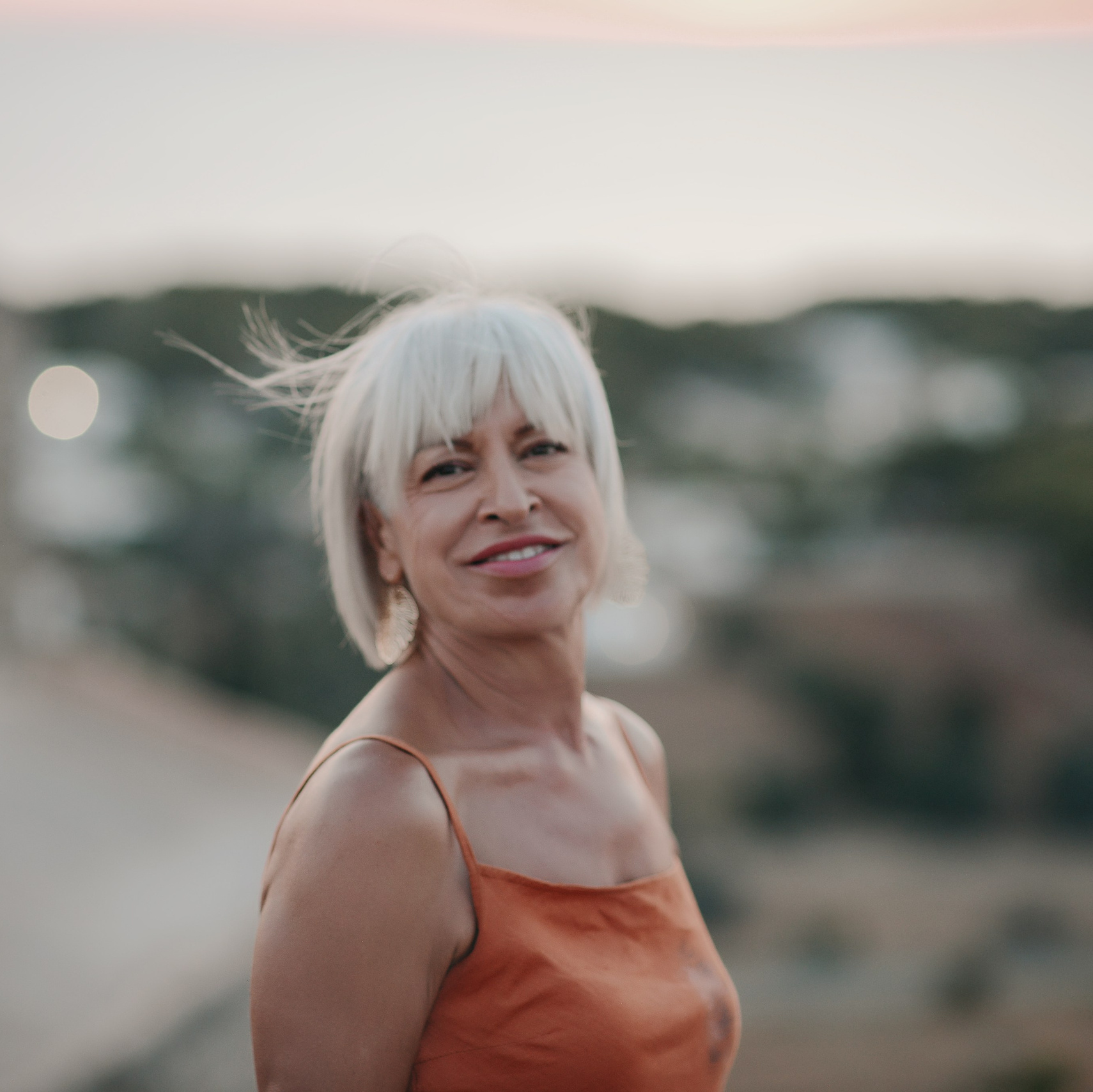 Portrait of a smiling woman with white hair at sunset, overlooking a southern Italian village.