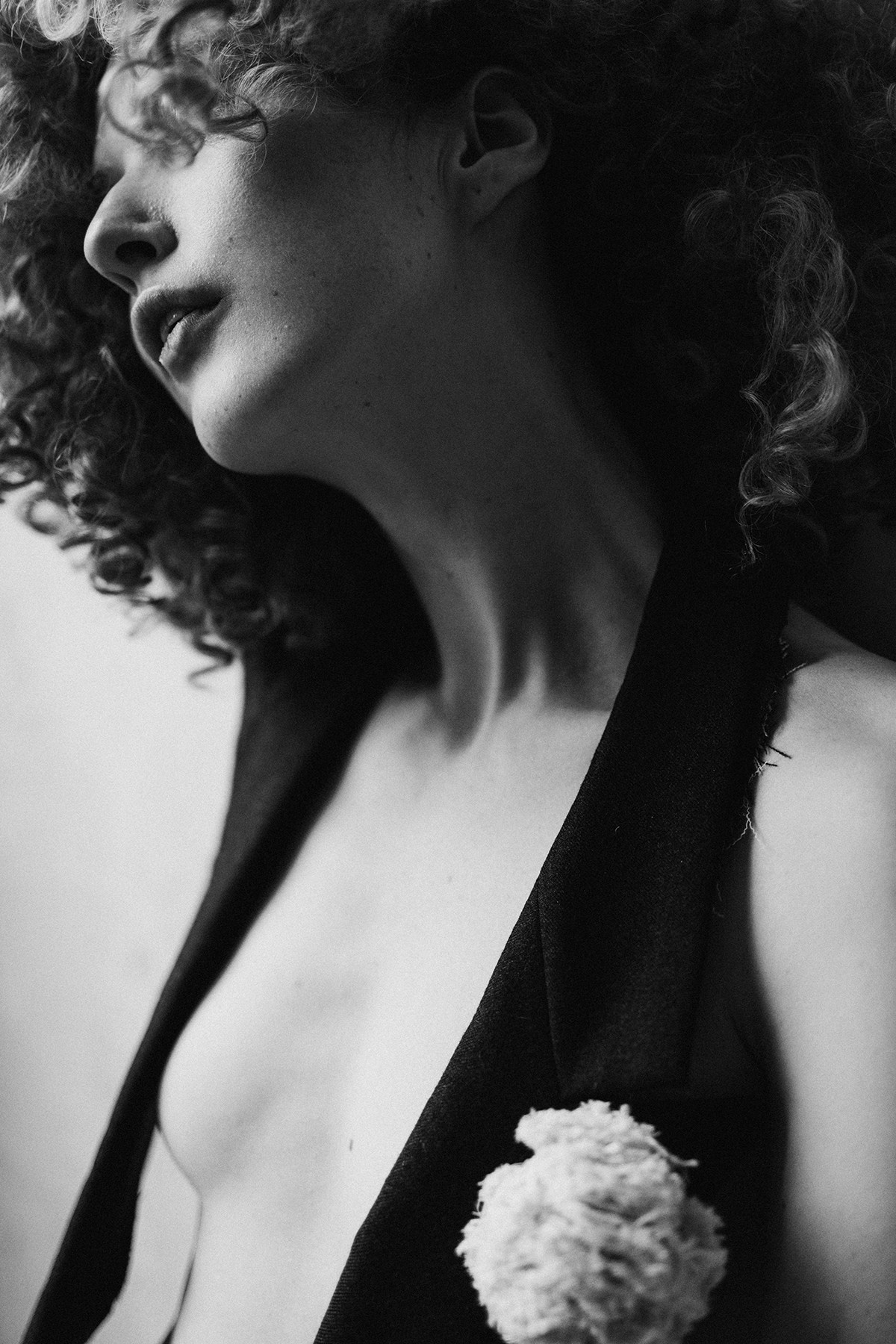 Black and white close-up of a woman reclining with her arms raised, her face illuminated by a shaft of light.