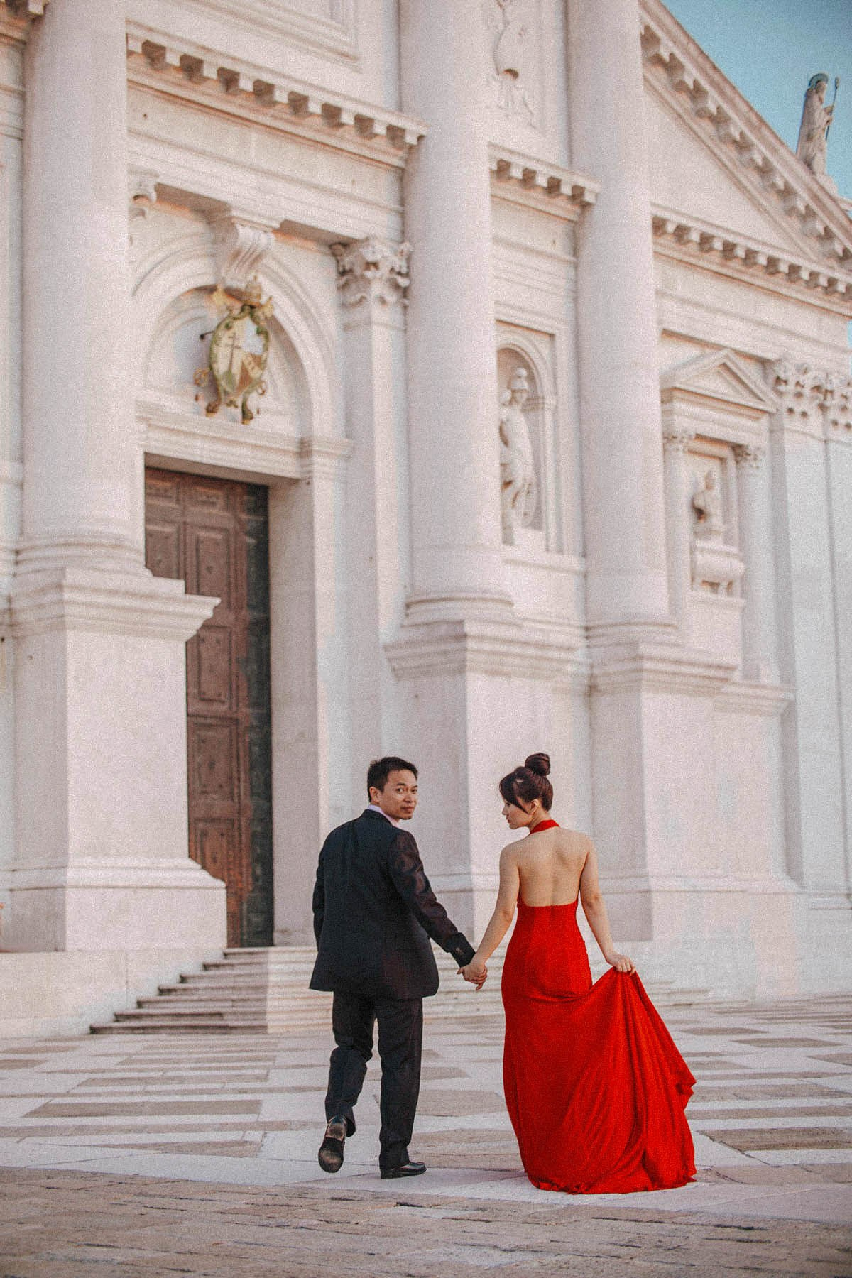 A stylishly dressed Thai couple walks across the empty plaza in front of the Basilica of San Giorgio Maggiore at dusk.