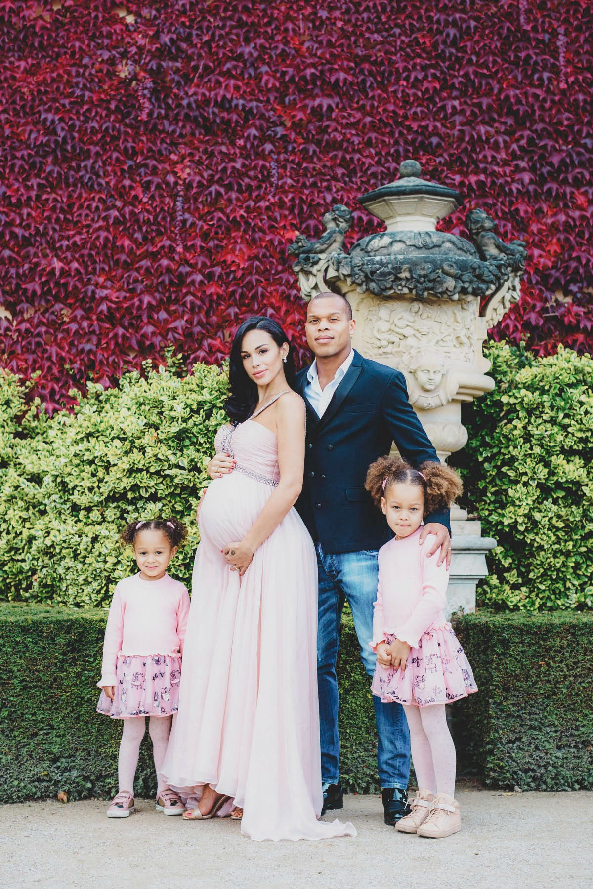 Family of four in pink and navy standing in front of a crimson ivy wall at Vrtba Garden, Prague