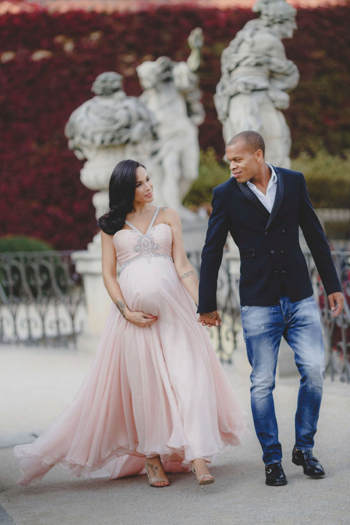 A couple walking hand in hand past Baroque statues, her pink chiffon gown moving
