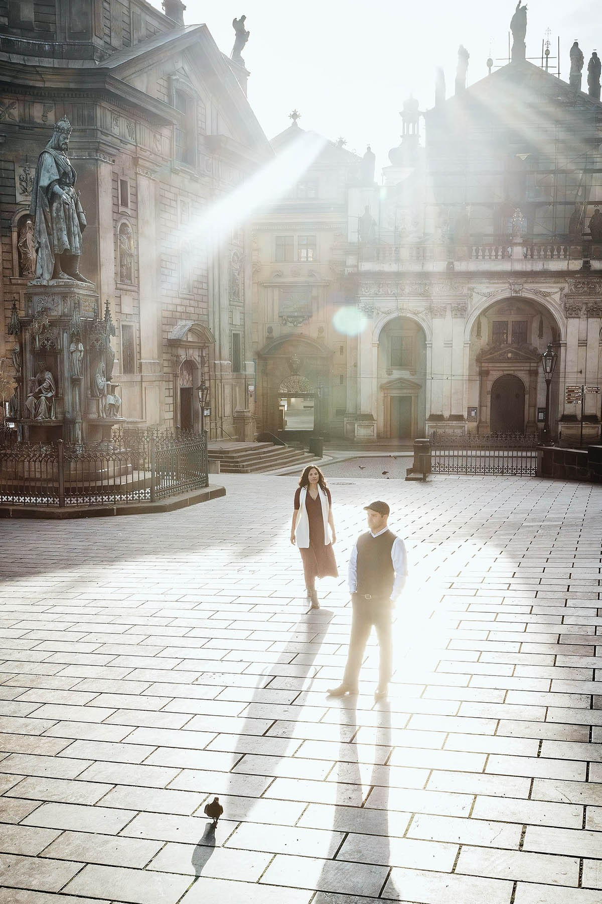Man waiting beneath the statue of King Charles IV in Křižovnické Square while his partner approaches during a sunrise photography session in Prague