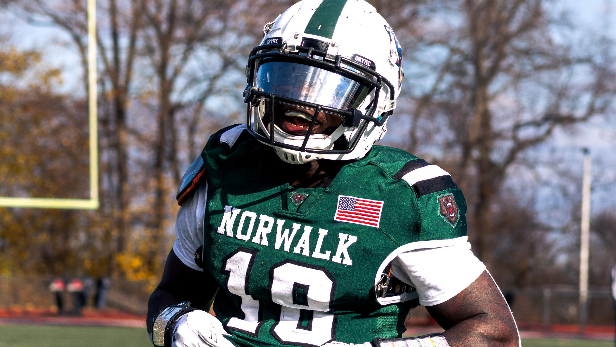 High school football player in a green uniform is moving down the field during an outdoor game.
