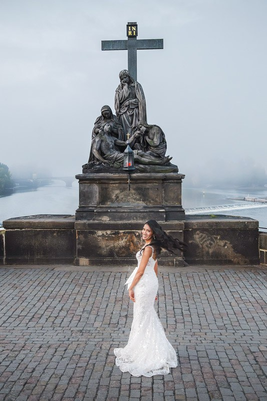 Bride spinning in her dress as a statue looms above atop a foggy Charles Bridge