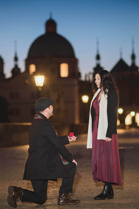 Candid engagement session — groom proposes on one knee to his partner atop the Charles Bridge at dawn, Prague — Kurt Vinion Photography