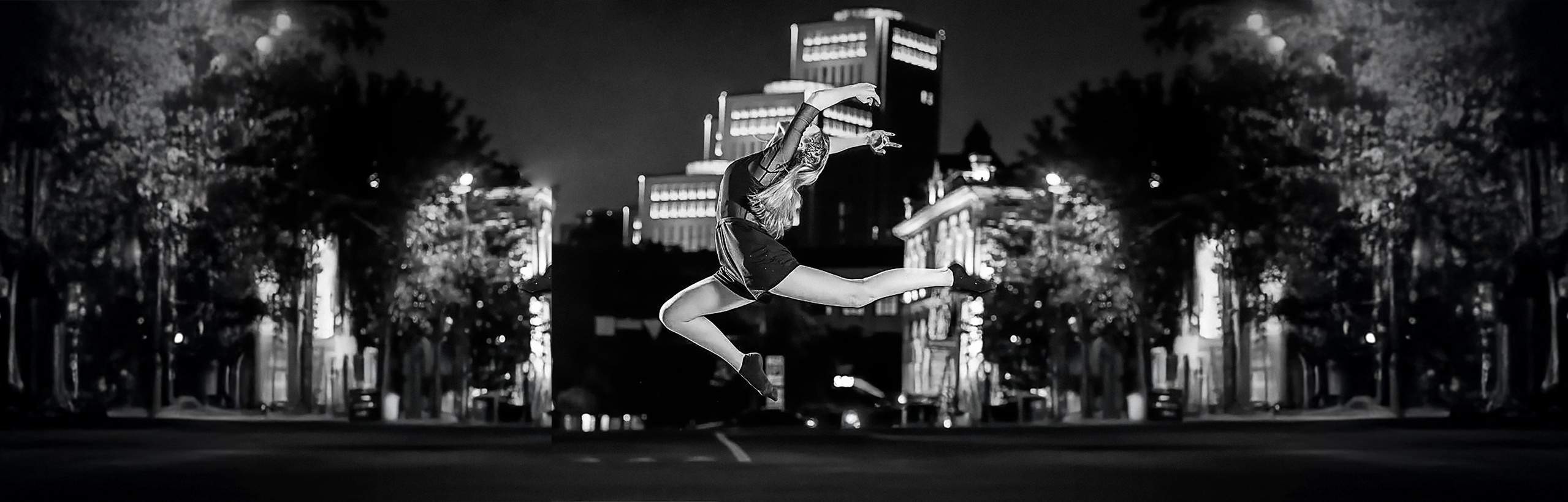 Black and white photo: a girl jumping against a city building at night. Professional photography in New Jersey