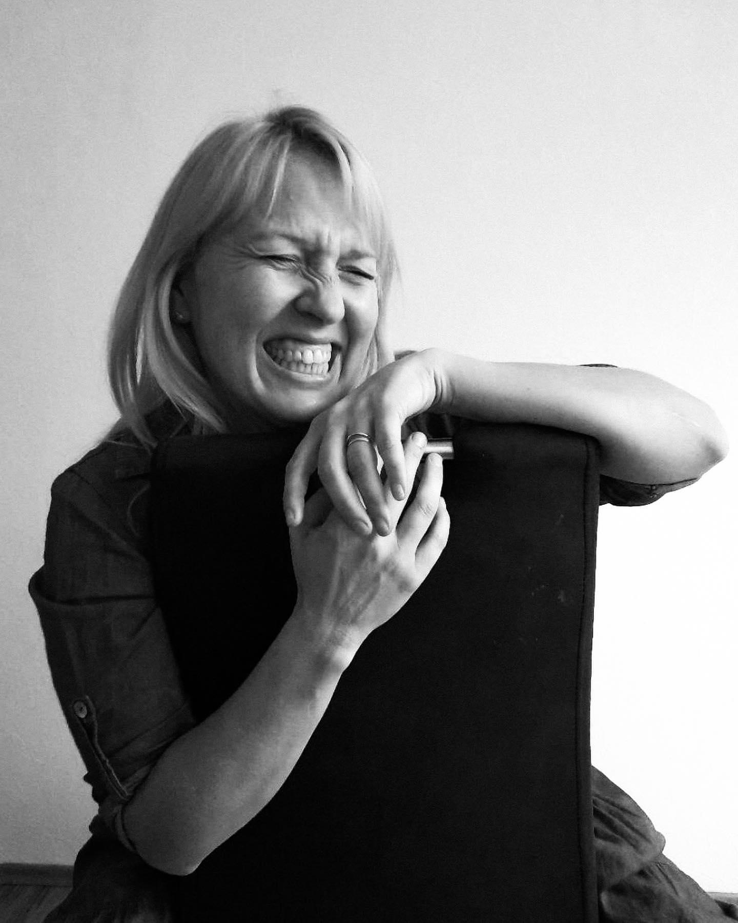 A black and white photograph of a lady smiling and sitting on a chair. Online photo shoot.