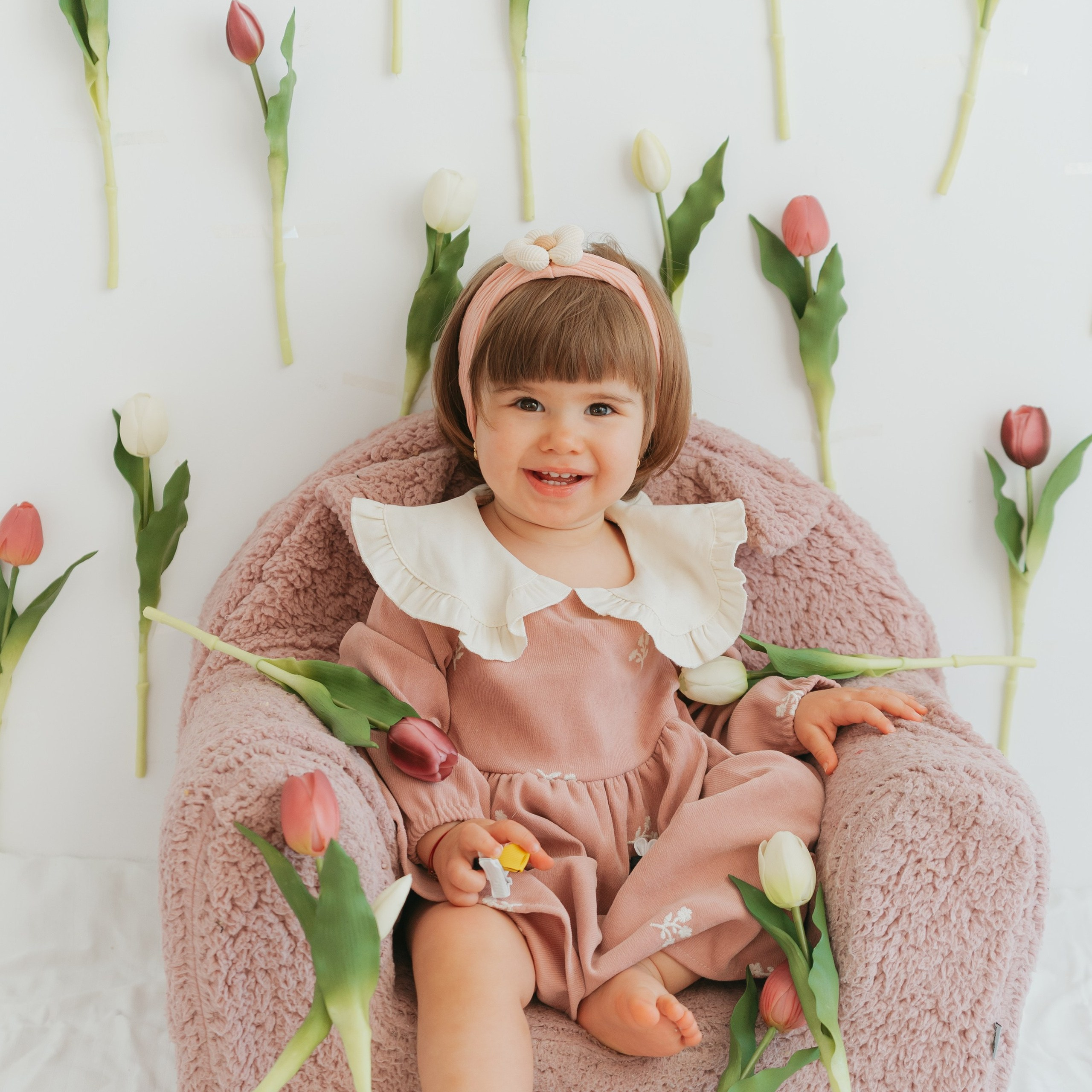 A child in a pink dress sitting beside spring tulips