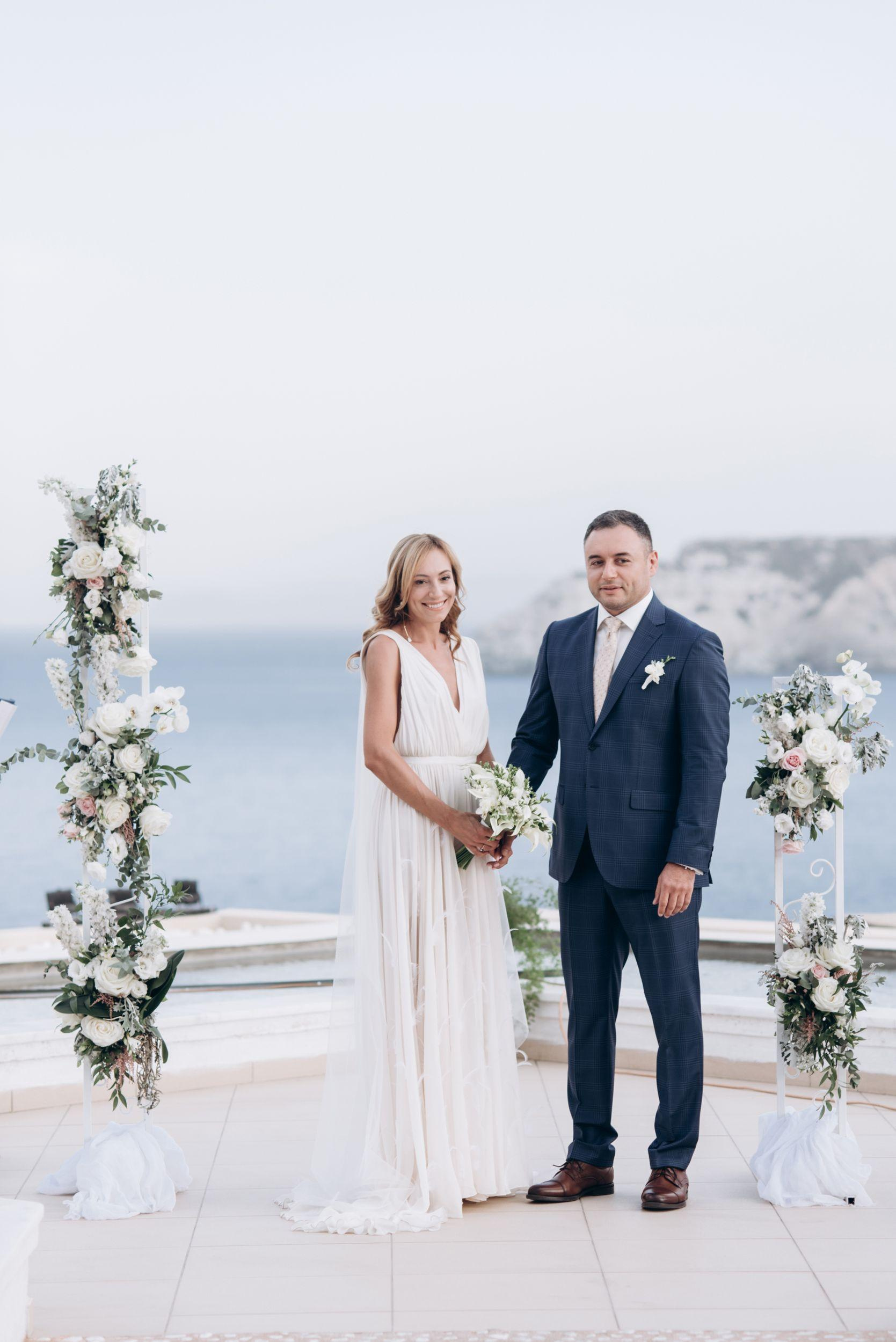 Невеста и жених на свадебной площадке в арке на фоне моря, на свадебной церемонии на Крите в Греции.
