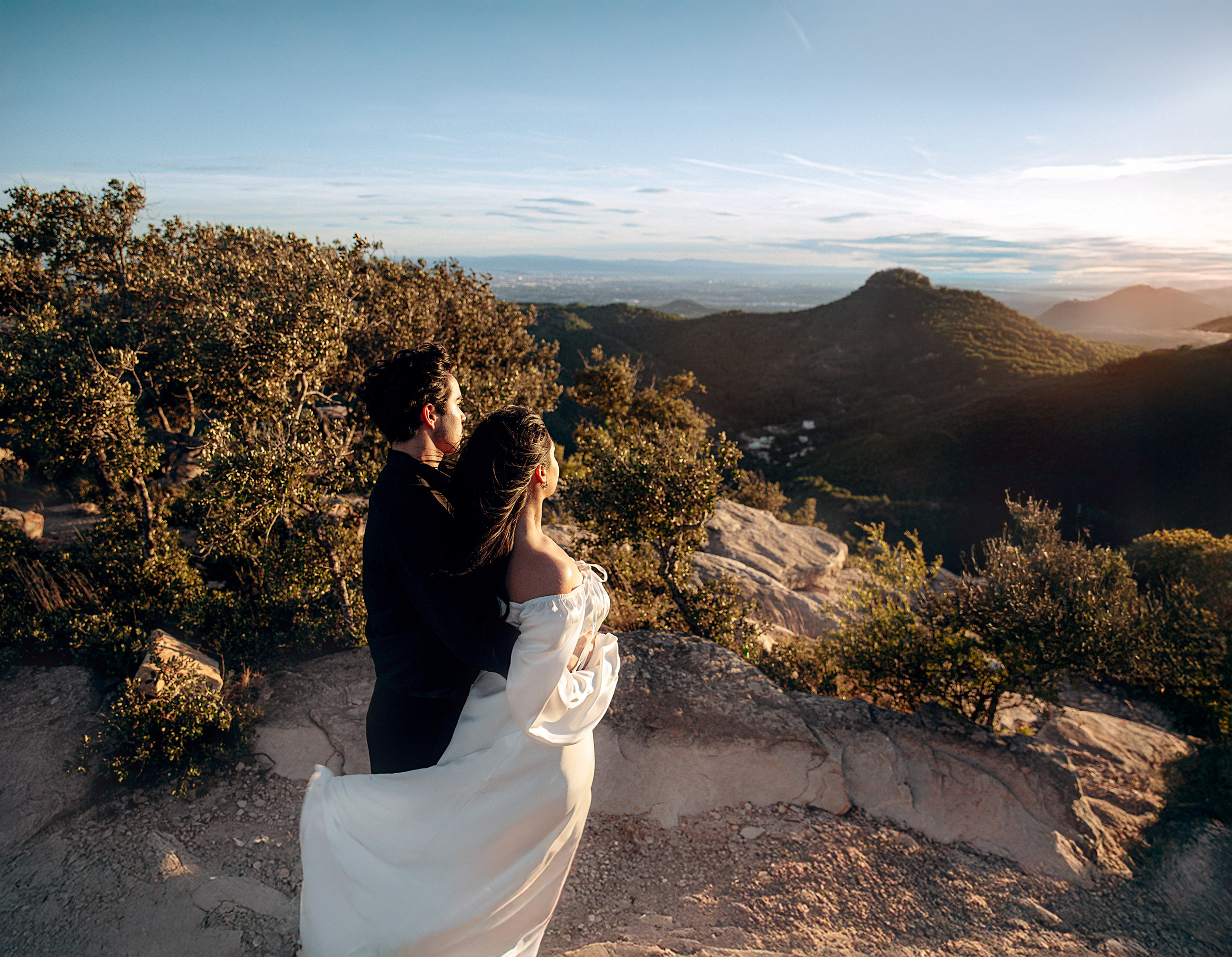 Couple holding each other among rocks and trees, with mountain views near Valencia.
