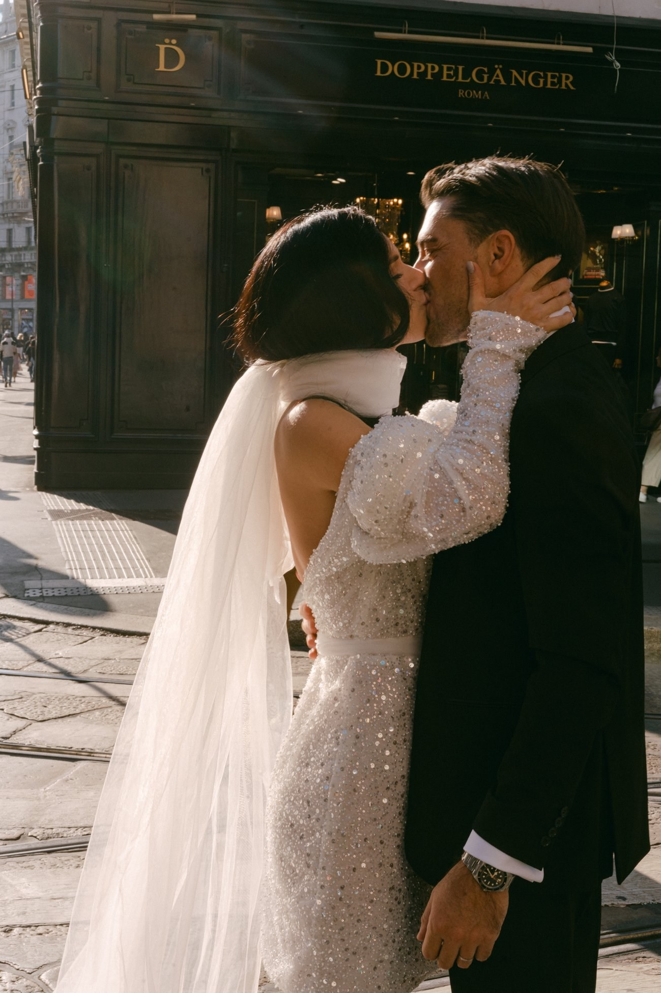 Bride and groom kissing on a sunlit cobblestone street, Milan, Italy