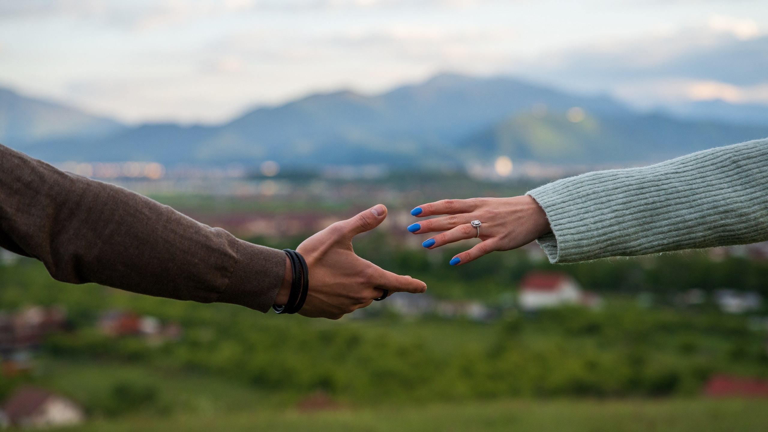 A couple reaching for each other’s hands with mountains in the background