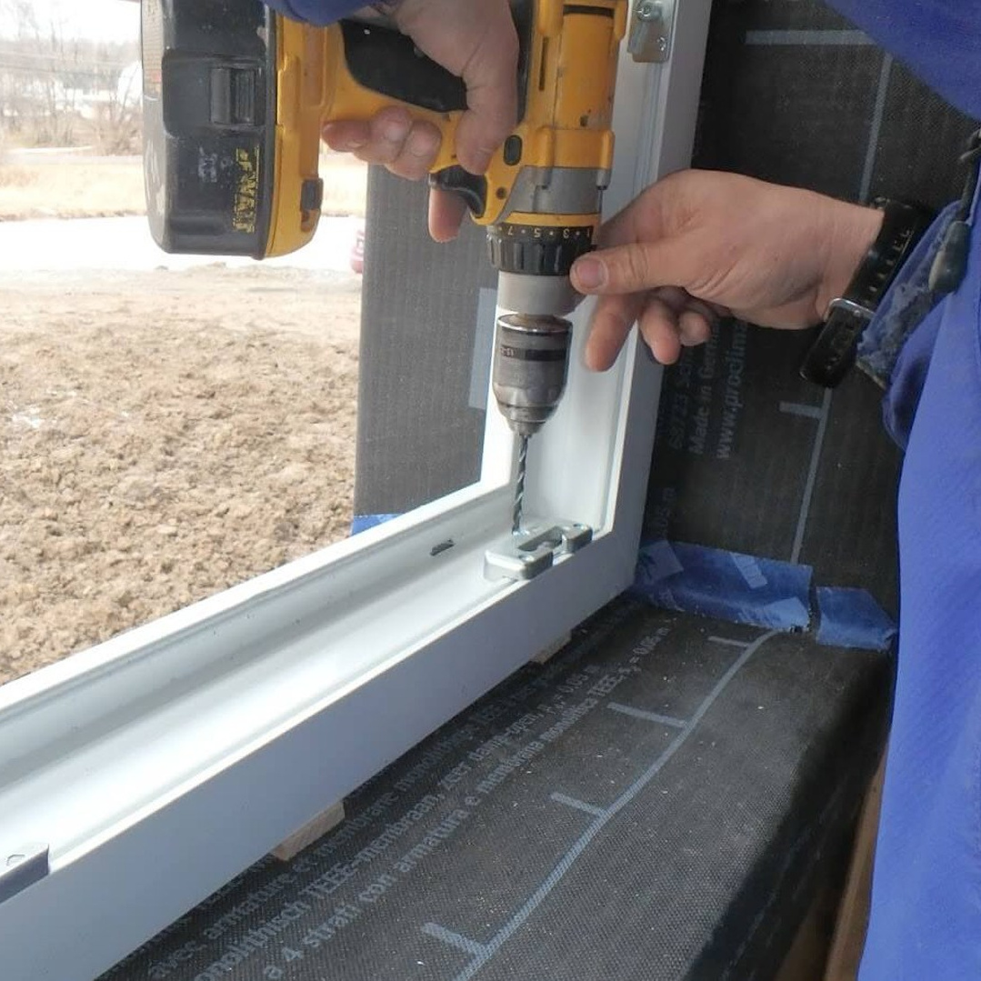 Монтажник производит установку белого пластикового окна.