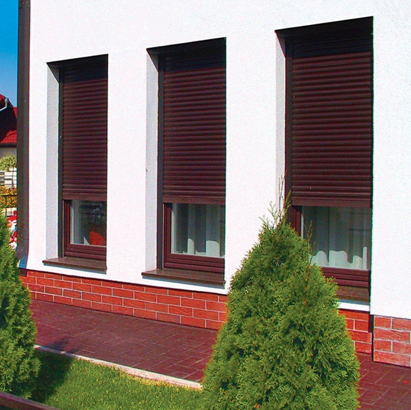 Три окна частного дома закрыты полуопущенными роллетами коричневого цвета.