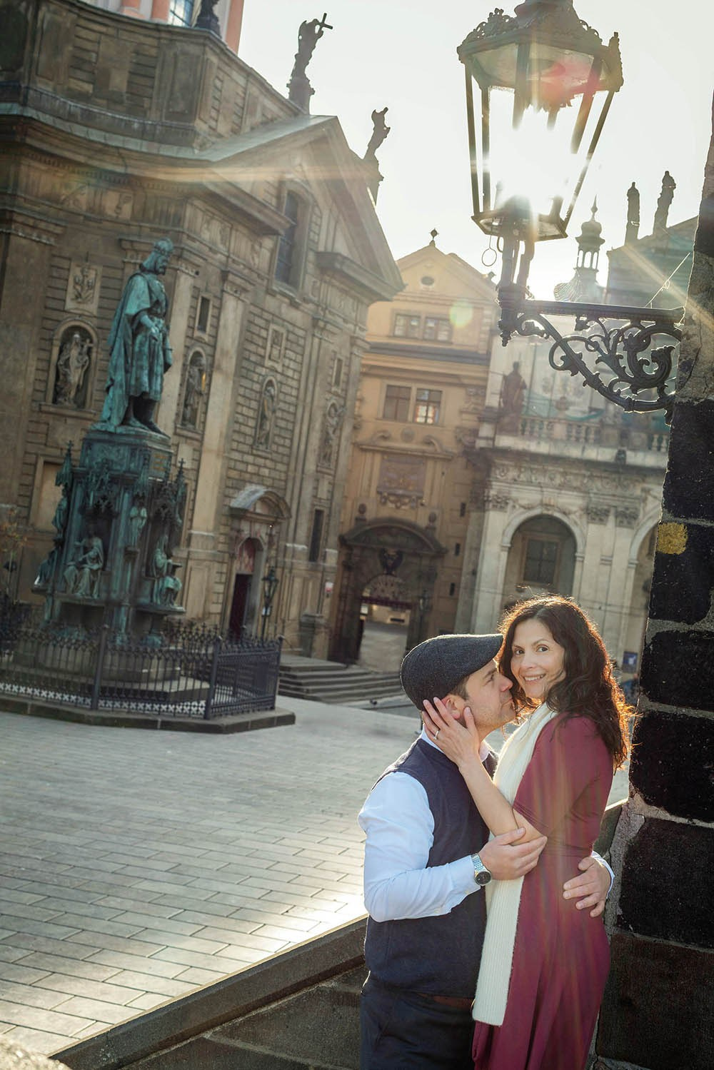 Smiling woman embraced by her partner beneath a historic gas lamp near the Gothic Old Town Bridge Tower on Charles Bridge in Prague