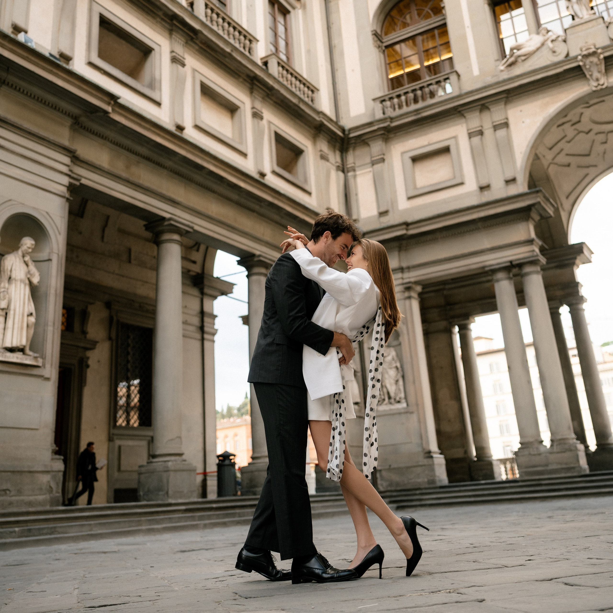 Editorial wedding portrait of a bride and groom surrounded by striking red florals in a luxury destination wedding setting in Milan. Bride and groom embracing outdoors between dramatic red floral arrangements on a stylish wedding terrace in Milan, Italy.
