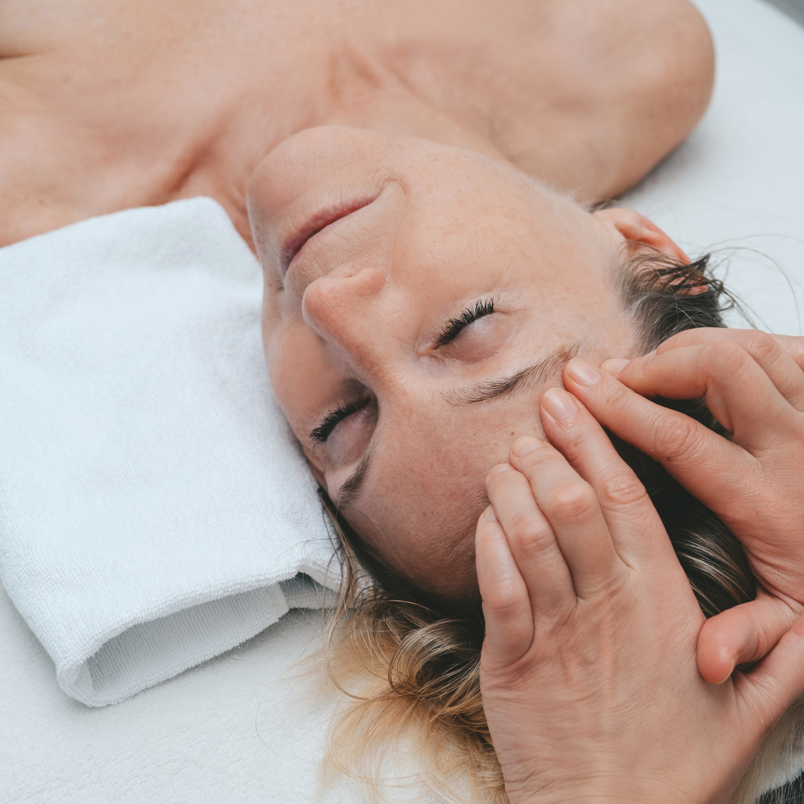 Eine Masseurin massiert eine Frau, die mit geschlossenen Augen liegt und sich entspannt