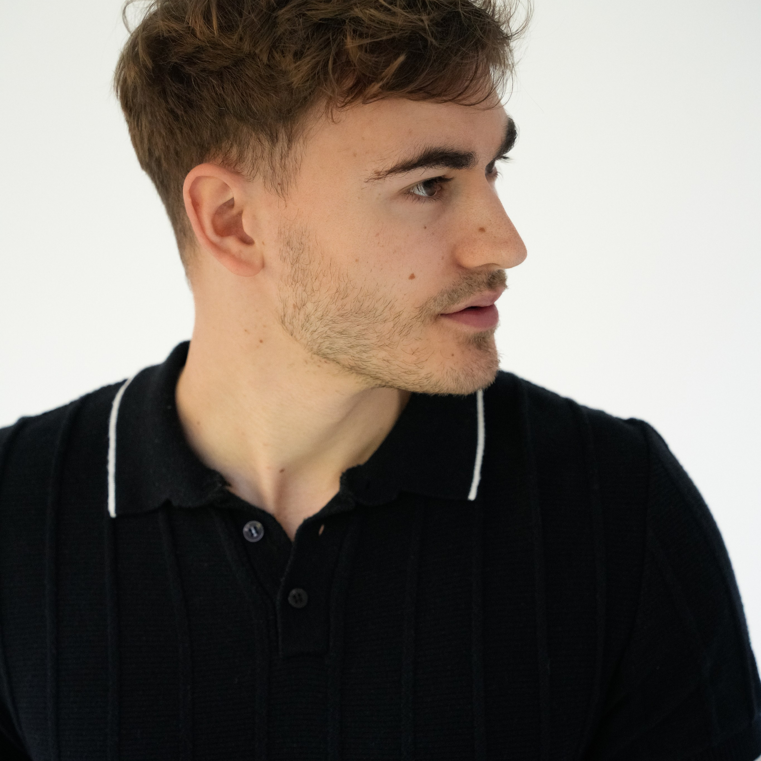 Professional headshot of young man in black polo shirt, studio portrait, Solihull