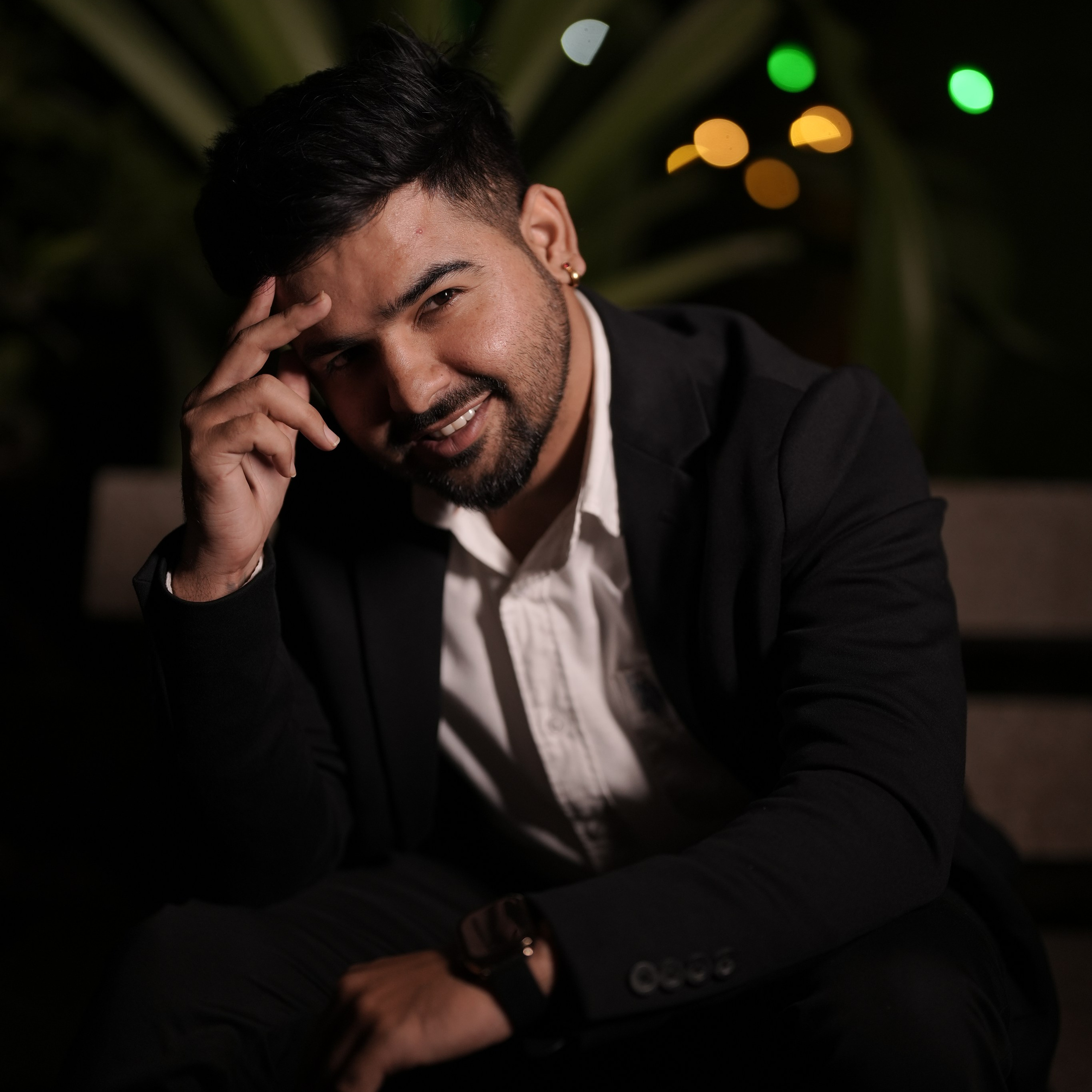 professional night portrait of a smiling man in a black suit posing with hand on head in Malleshwaram, Bengaluru