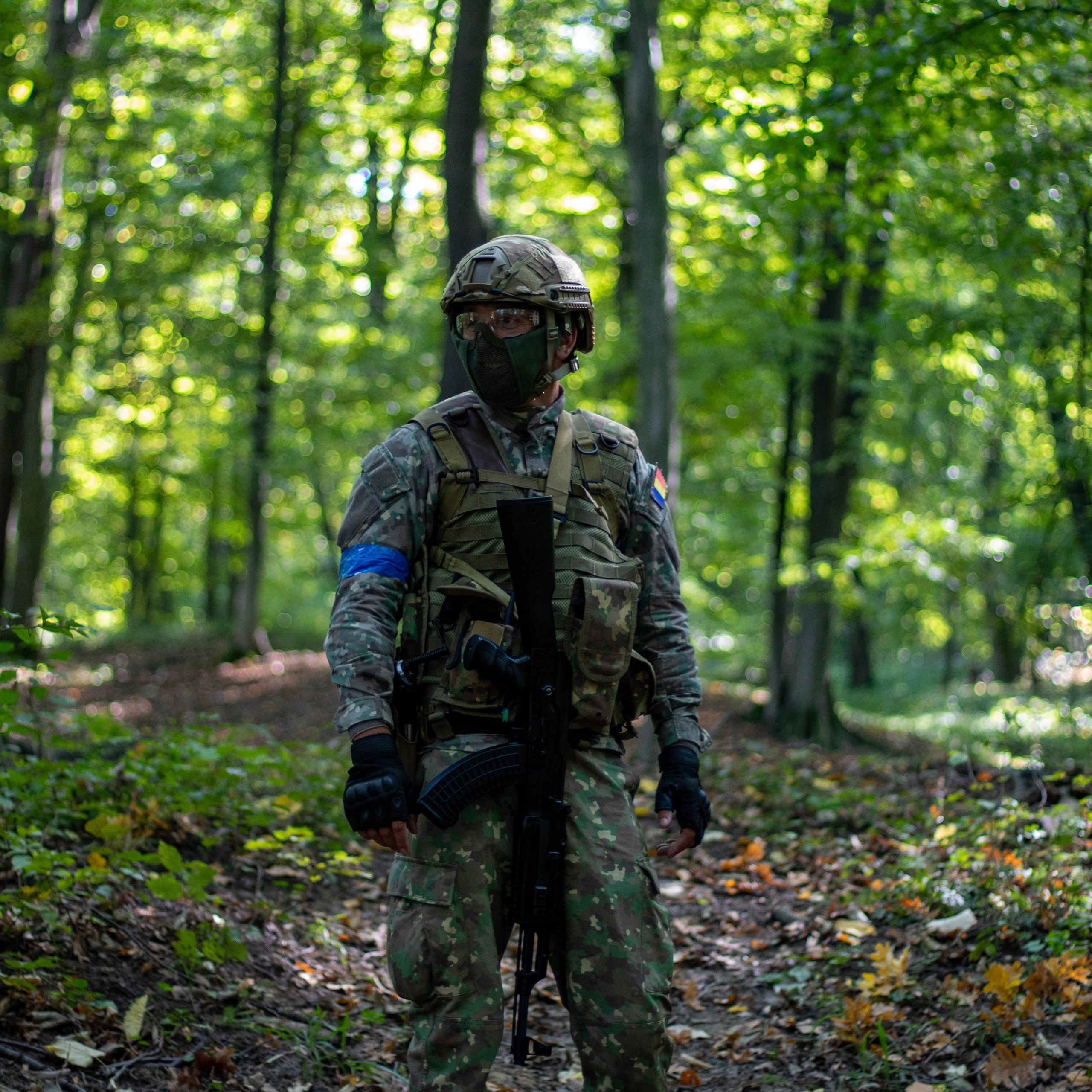 Airsoft player in tactical gear navigating through green woodland