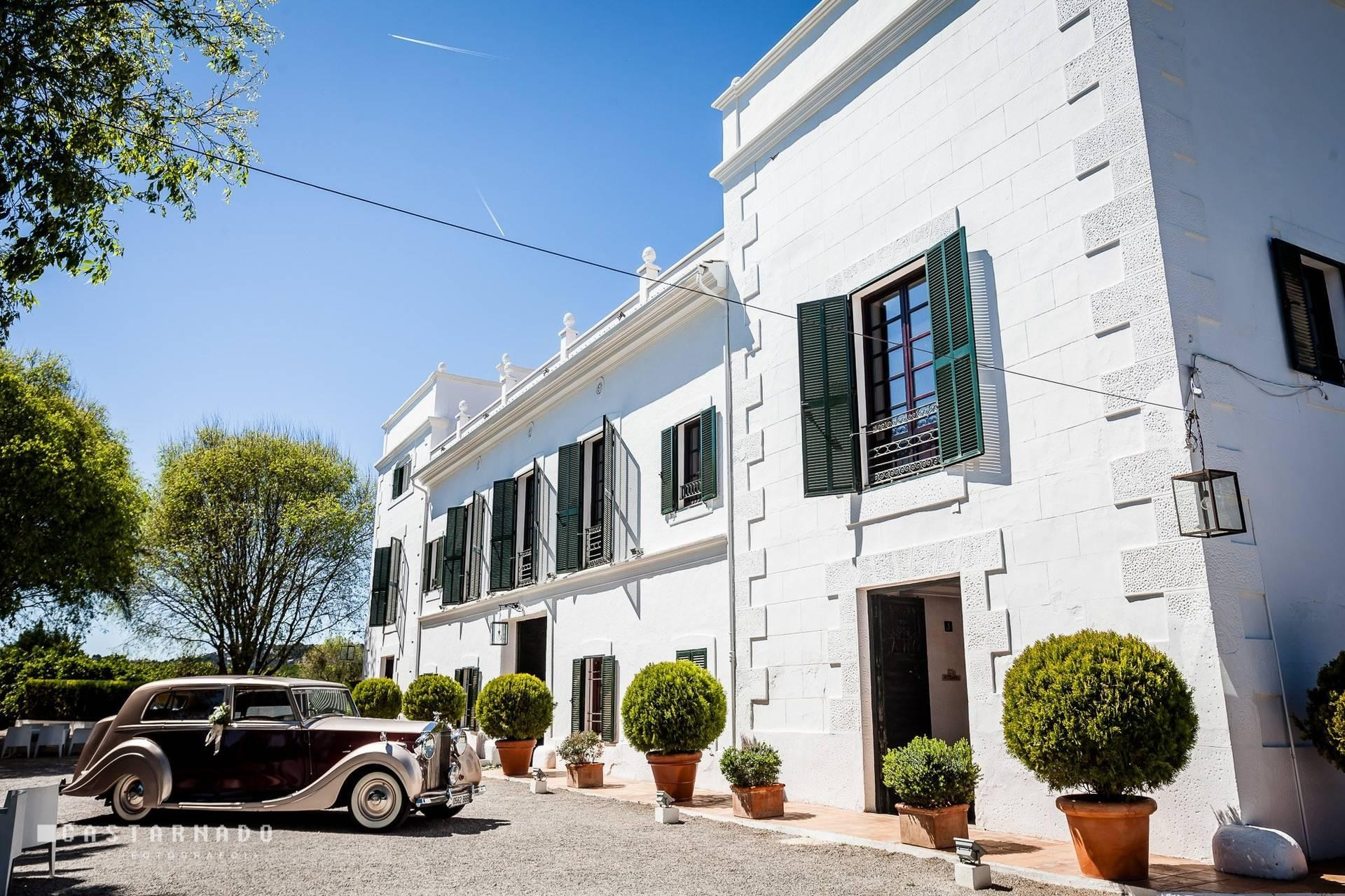 Vintage wedding car outside Masía Aldamar’s white façade with green shutters and potted topiary.