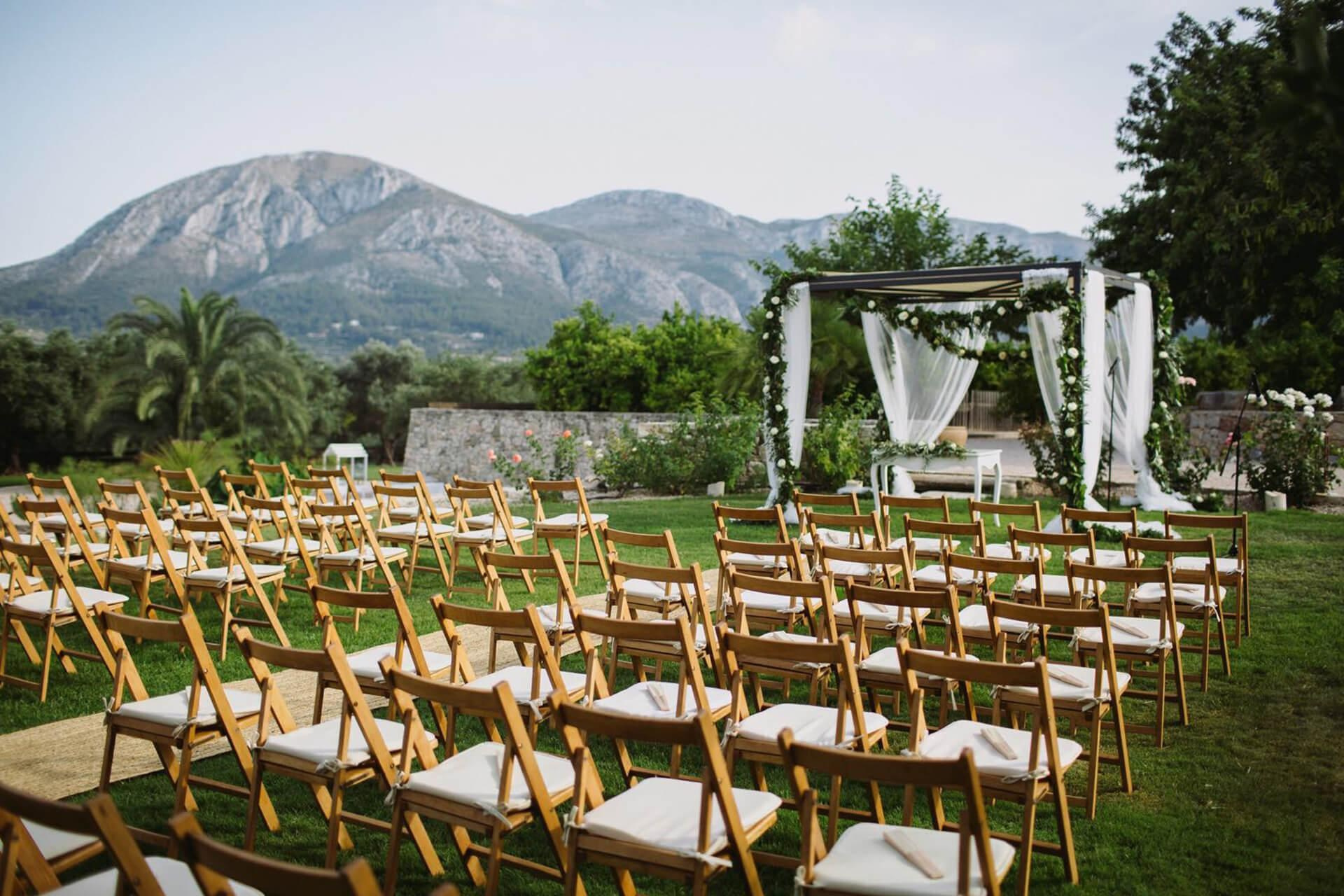 Garden wedding ceremony setup at Casa Benigalip, with wooden chairs, a white-draped floral canopy and mountain views.