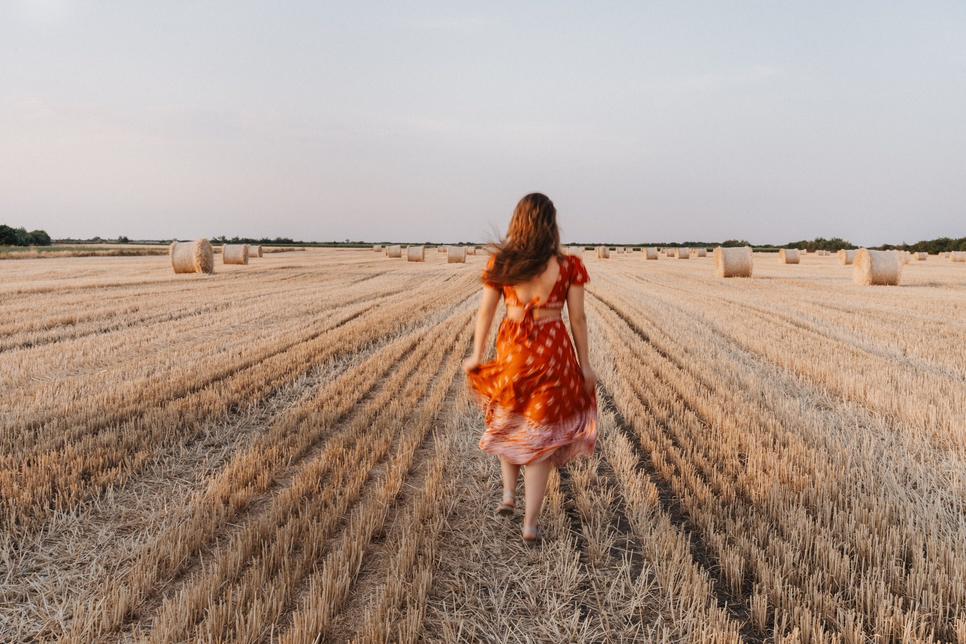 devojka u crvenoj letnjoj haljini trči kroz polje pred kraj leta, zamućen kadar u pokretu