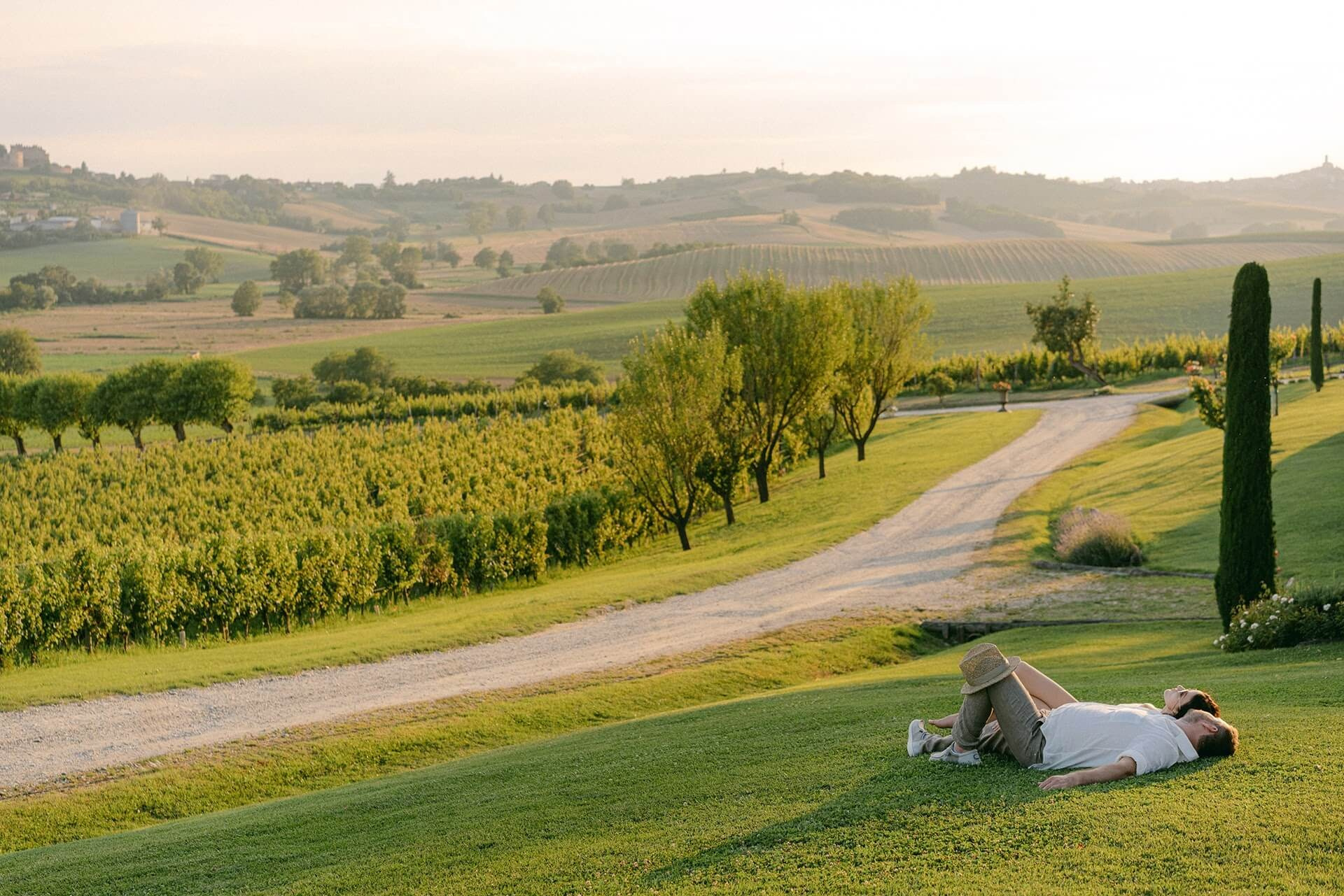 Пара отдыхает на холме в Пьемонте на закате, панорамный вид на виноградники Ланге и романтичная атмосфера итальянского лета