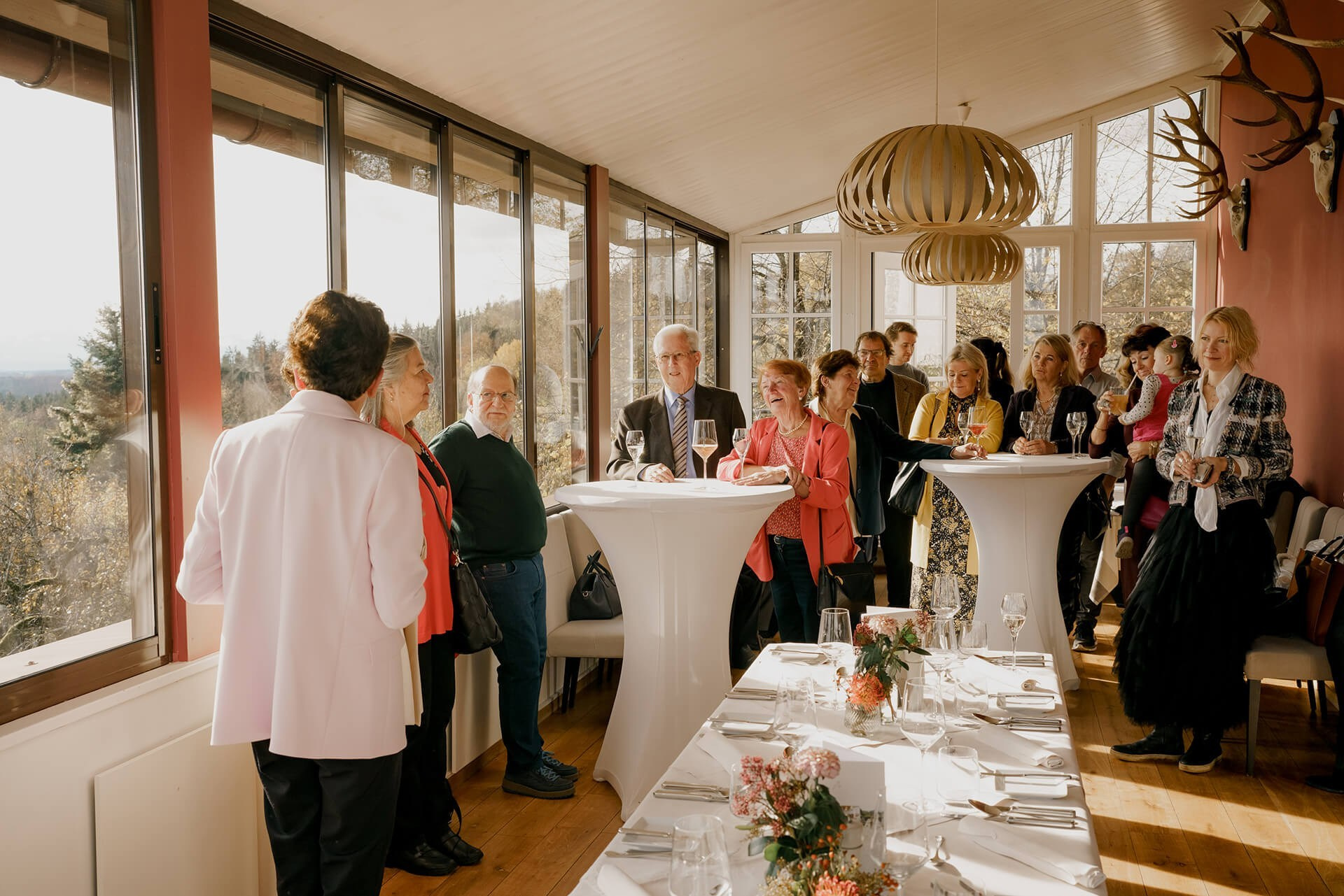 Corporate holiday reception in Munich. Guests gather around cocktail tables in a sunlit venue. Professional event photography for Christmas events