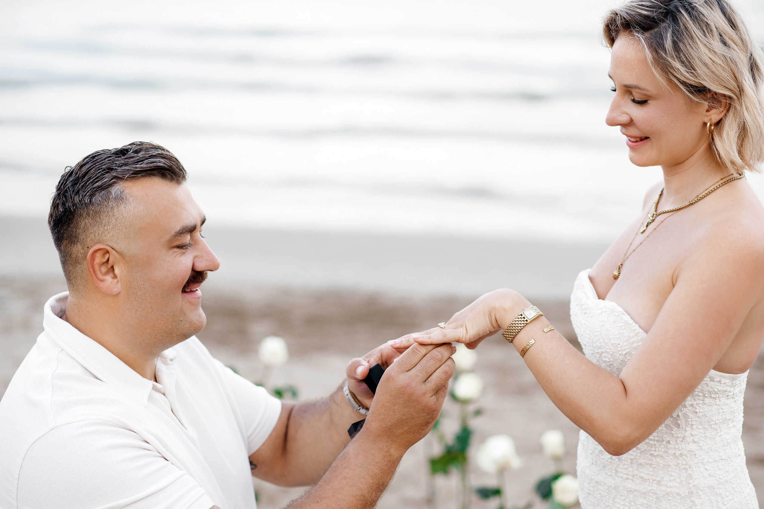 Romantic beach proposal in Alicante, Spain, with a man placing an engagement ring on his partner’s hand by the Mediterranean Sea