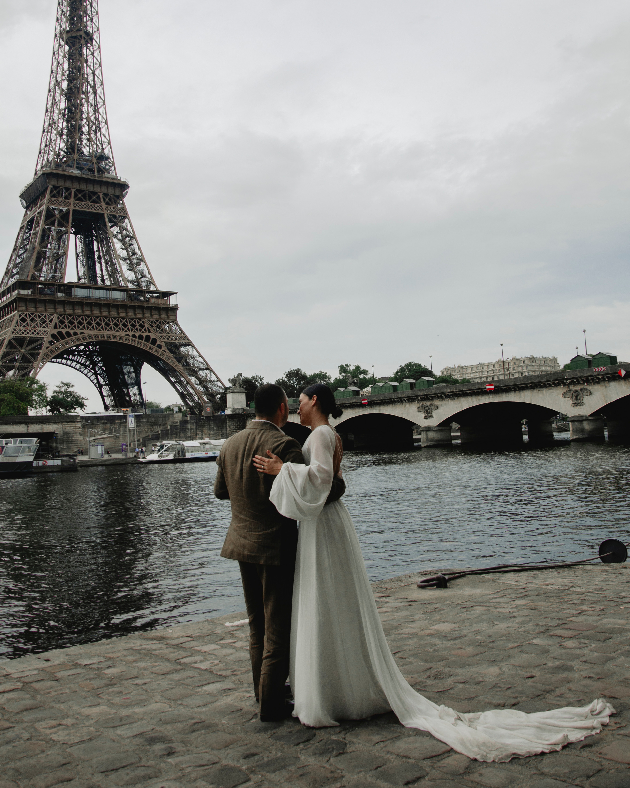 Молодожёны стоят на набережной Сены на фоне Эйфелевой башни