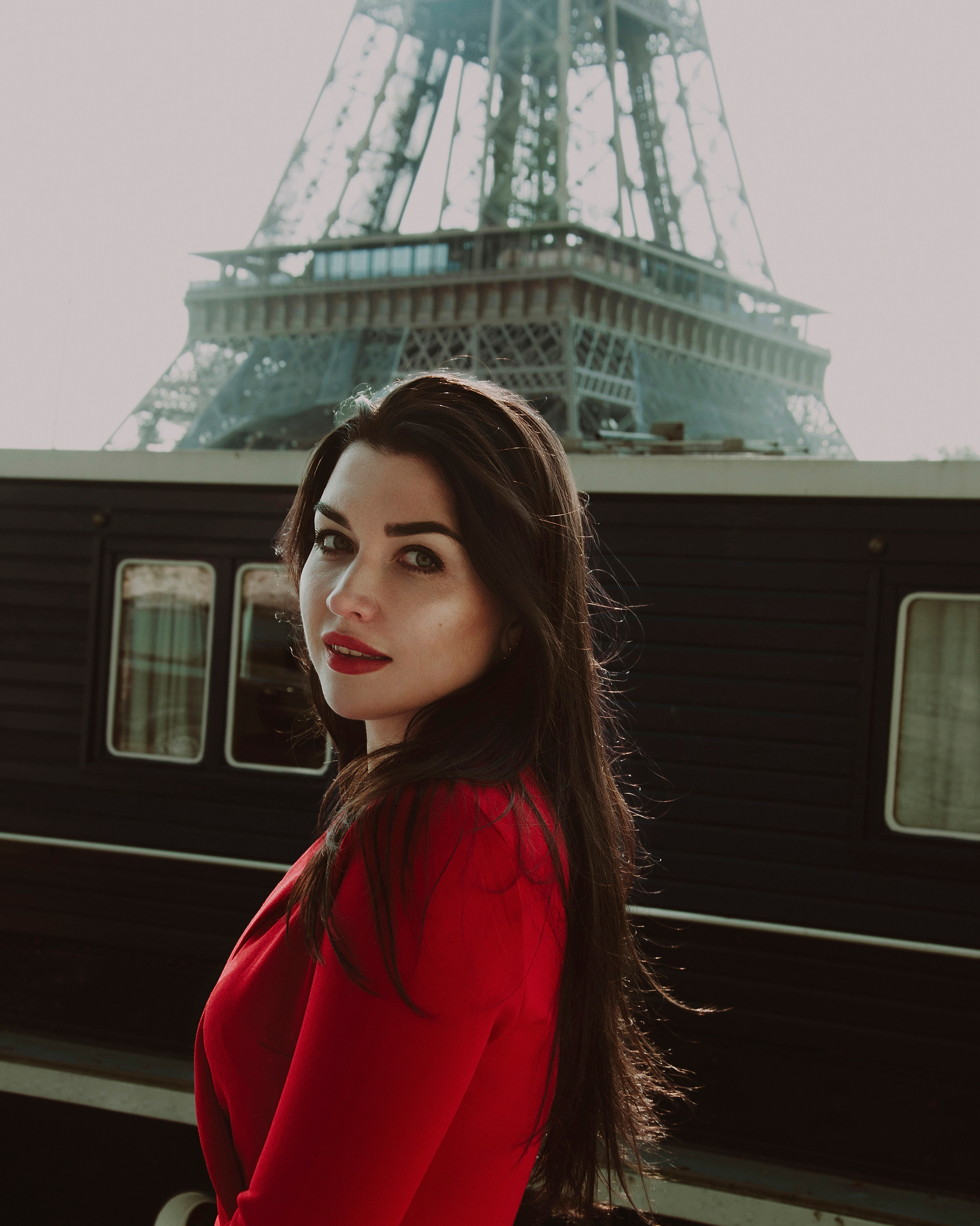 Девушка в красном платье стоит на набережной Сены на фоне Эйфелевой башни