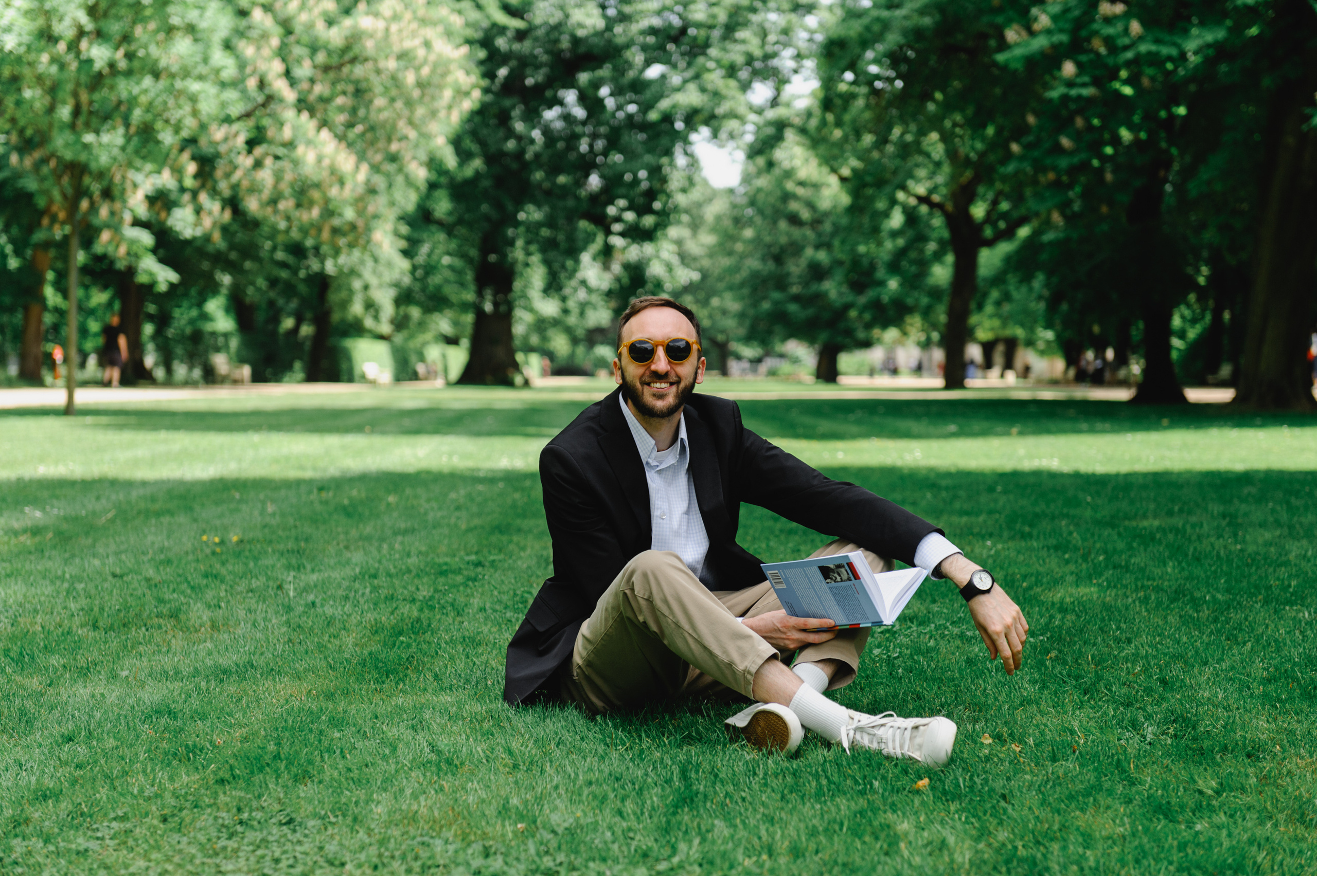 Cultural scholar Dmitry Solodkiy reads the book "Existential Psychotherapy". He sits on the grass, smiles, and looks at the camera.