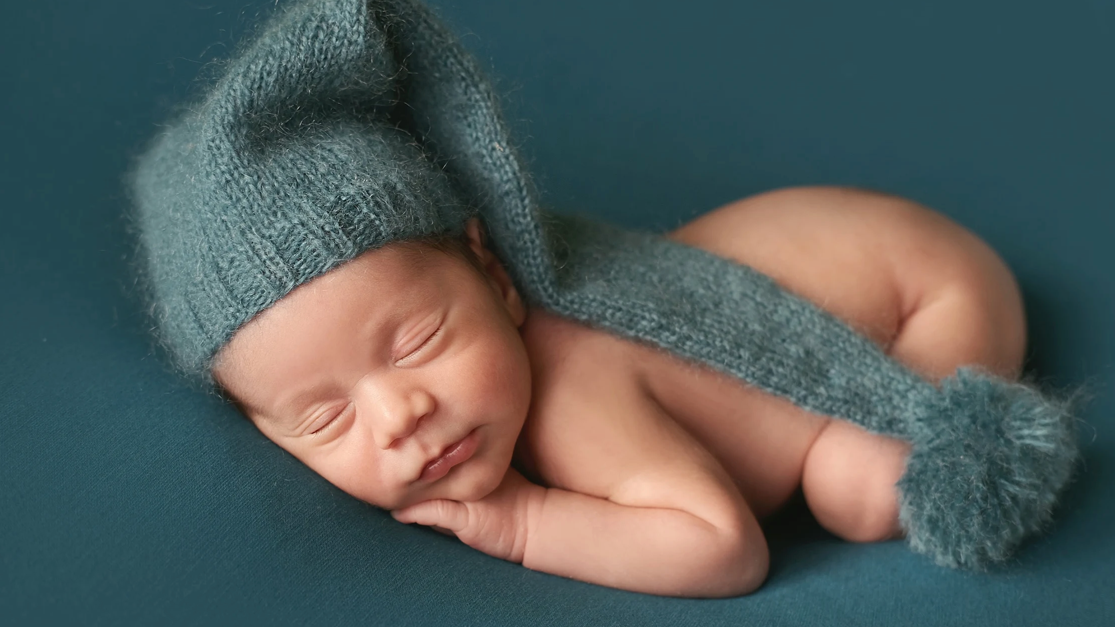 Newborn baby sleeping in hand-knitted bonnet with pom-pom