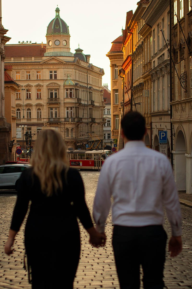 A couple holding hands as a tram passes near Charles Bridge in Prague at sunrise