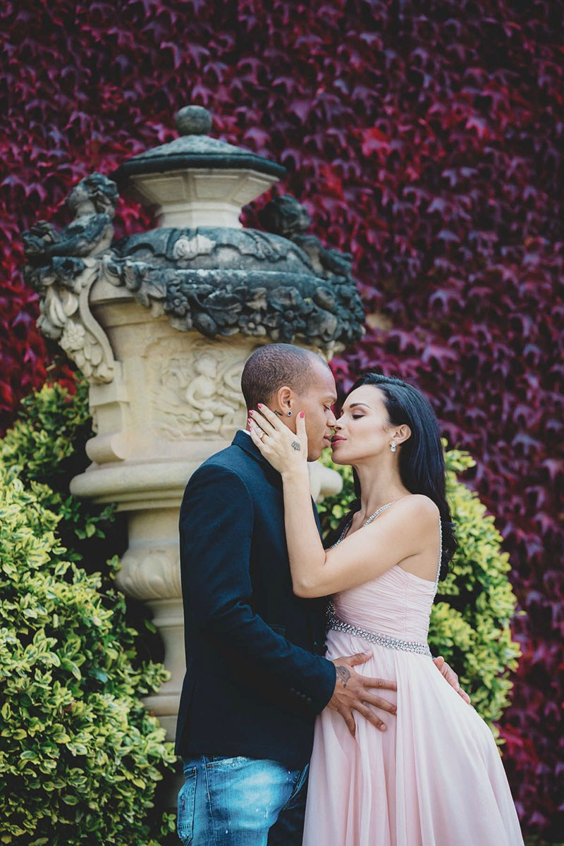 Expectant couple about to kiss beside a stone urn at Vrtba Garden