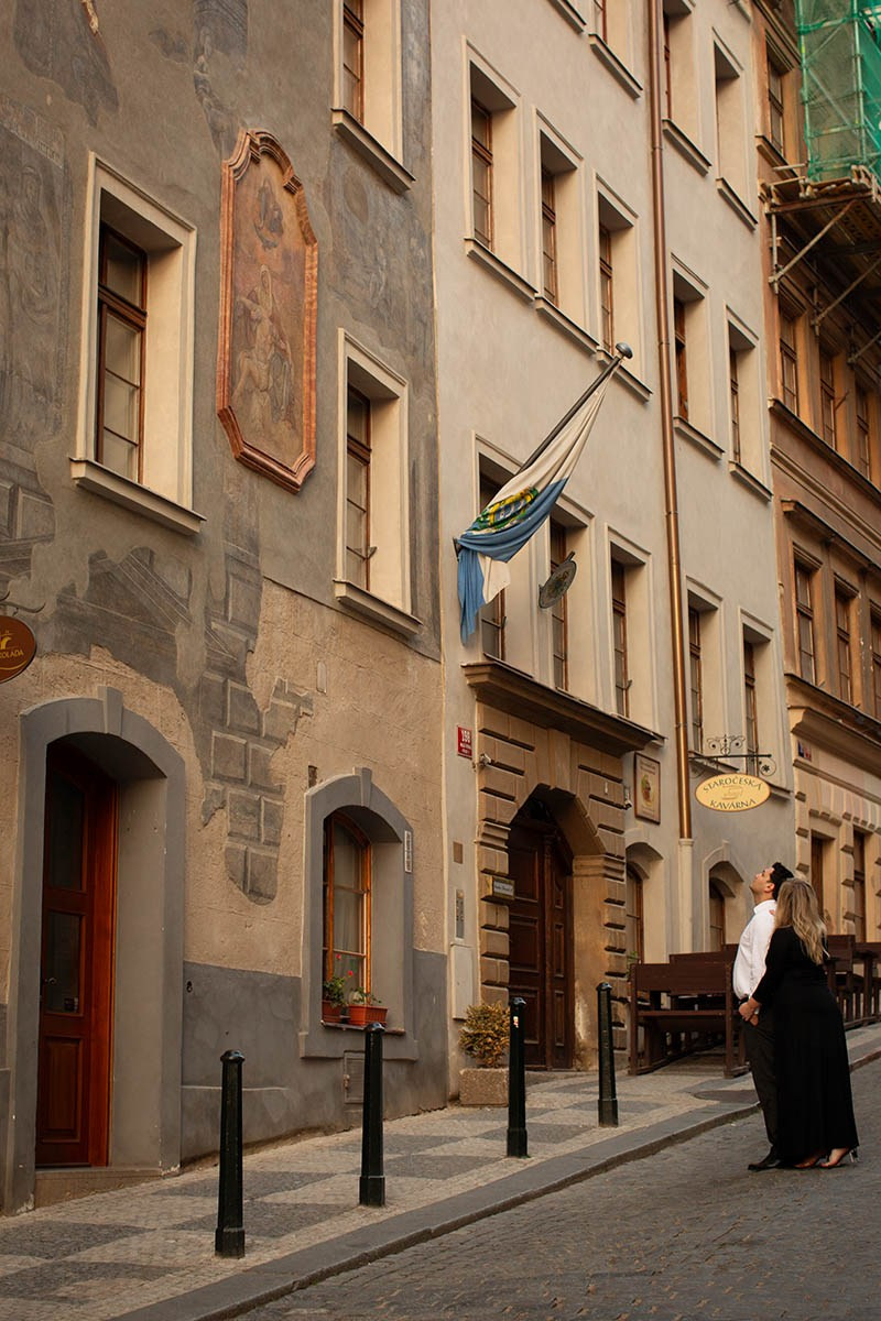 An American couple observing a medieval fresco on a historic building in Prague during early morning light