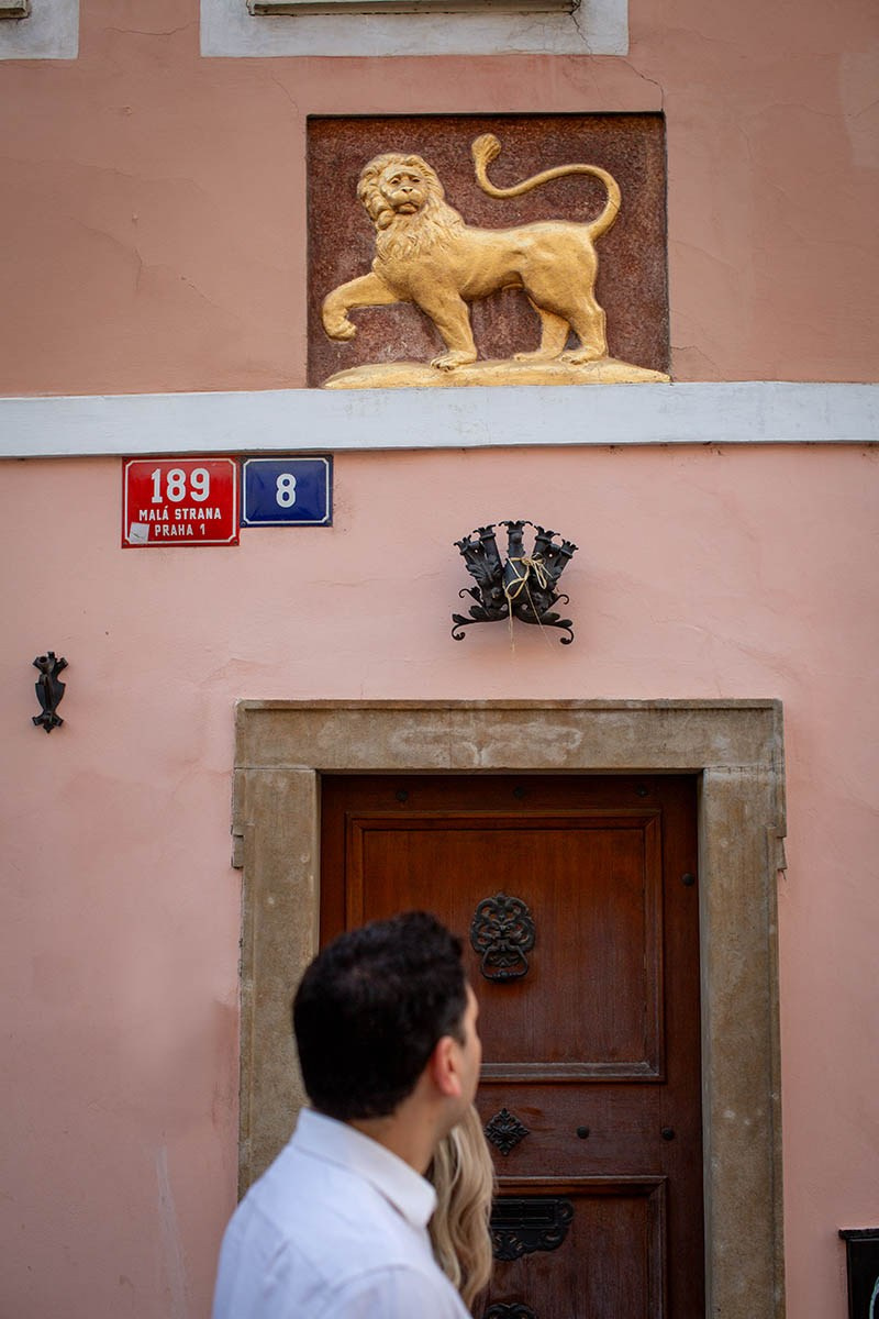 A couple admiring a historic house with a golden lion above the doorway in Malá Strana, Prague