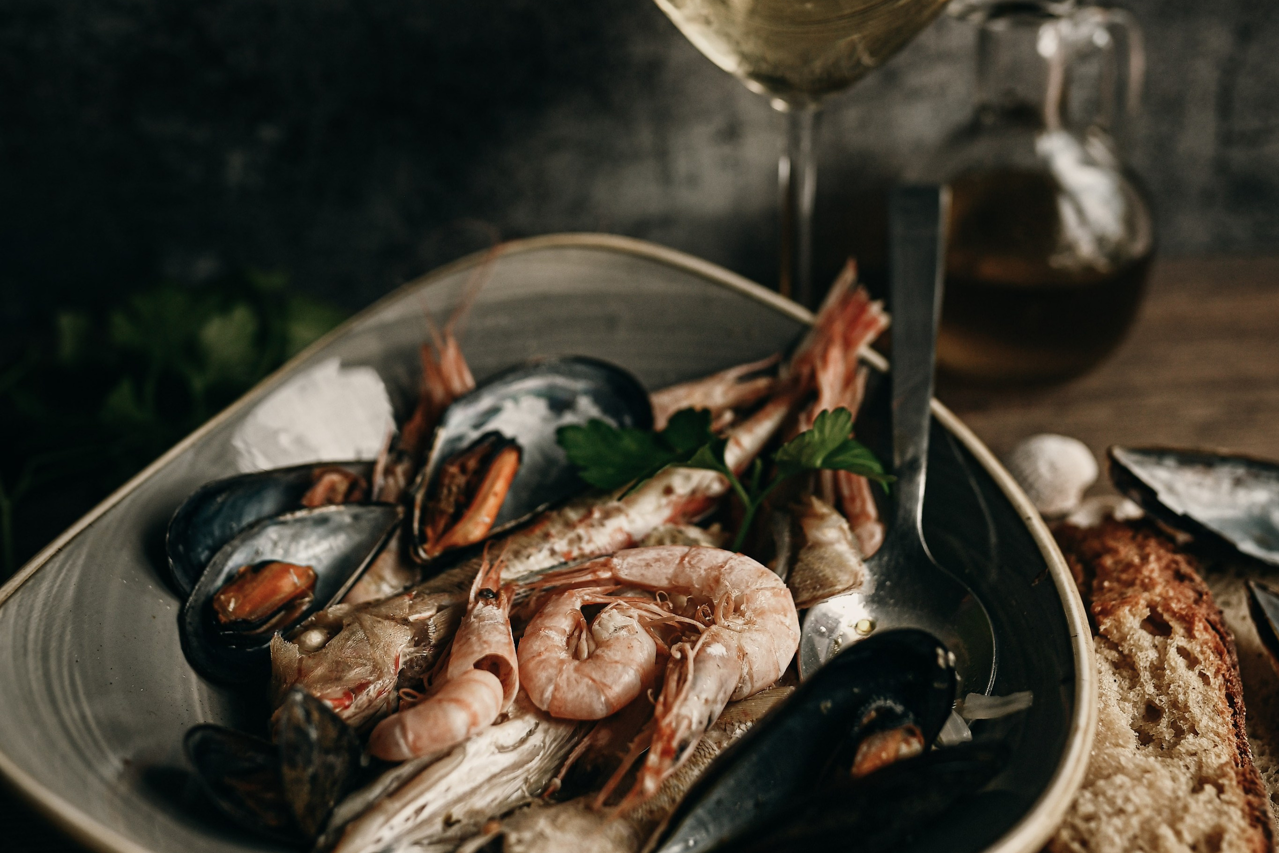 A plate of shrimp, mussels, and fish served with toasted bread and a glass of white wine. A beautifully styled traditional seafood dish from Salento.