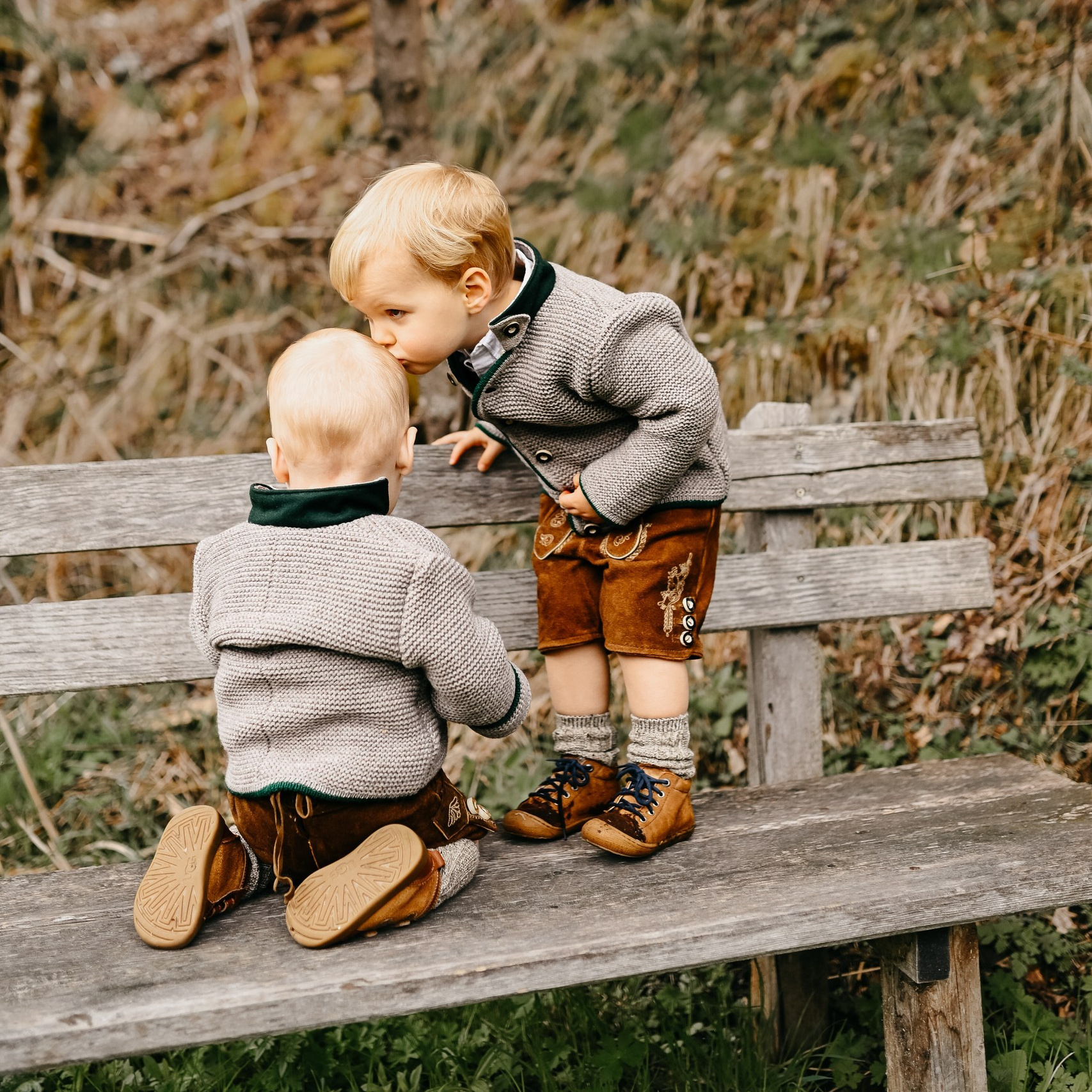 Kinder auf einer Bank im Wald - ein Bruder küsst den anderen auf den Kopf