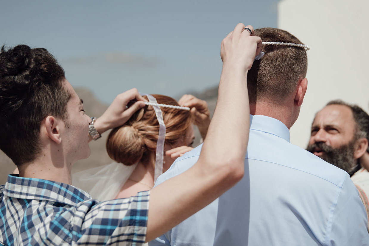 Свидетель держит венки над головами венчающейся пары во время венчания на Крите. Свадьба в Греции.