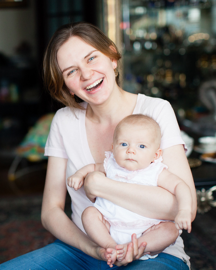Mother is laughing while posing to photographer with her small new born baby 