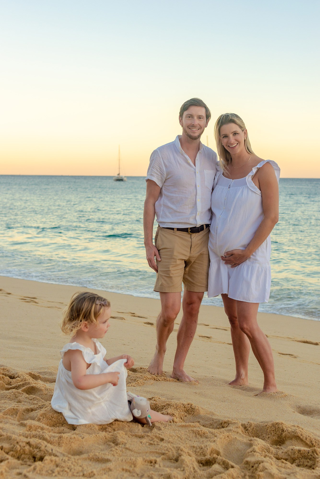 Pregnant couple dressed in white on the beach at sunset in Los Cabos