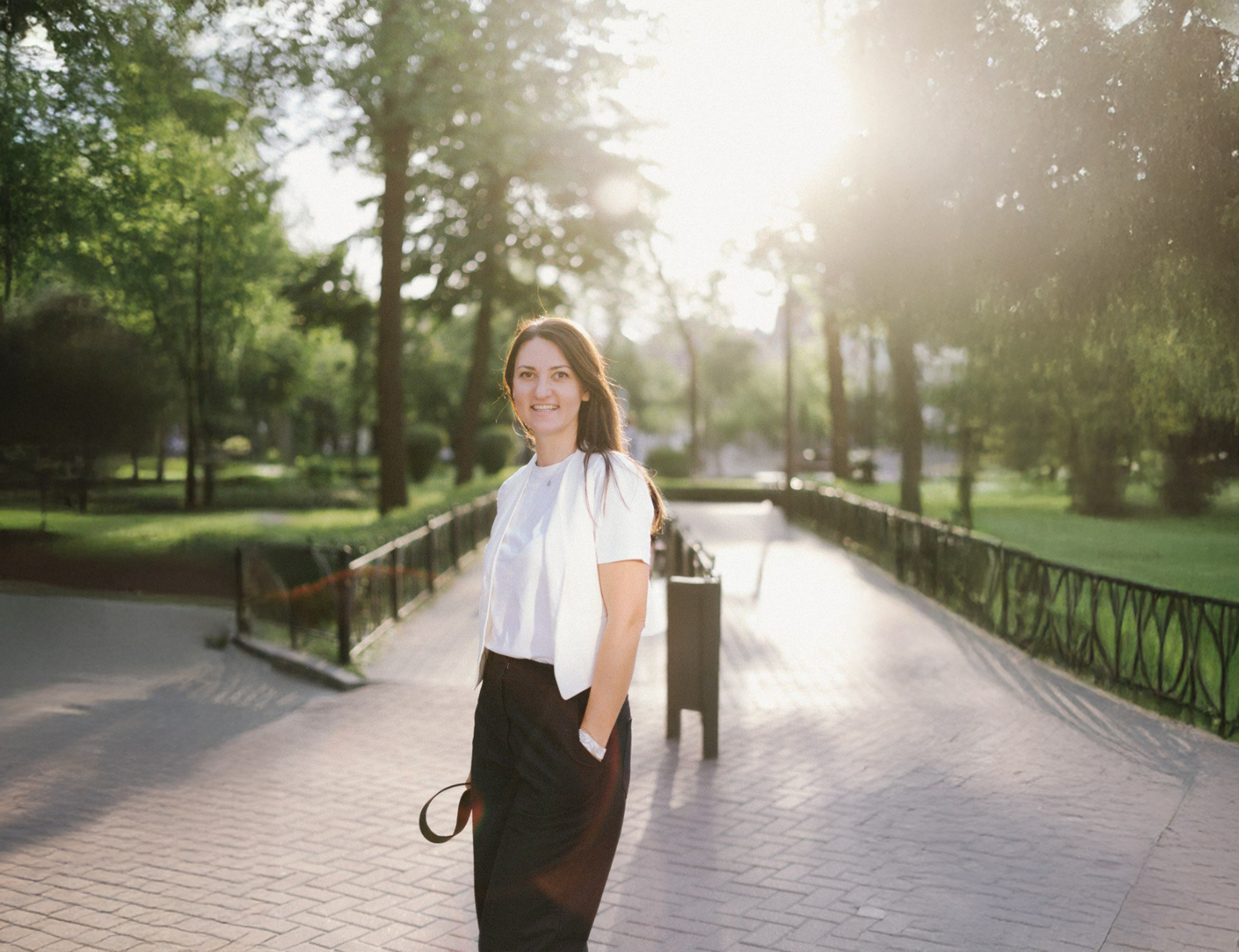 Wedding photographer walking through a sunlit park in Spain, carrying camera gear and smiling confidently. Natural behind-the-scenes portrait reflecting a calm and professional wedding photography experience.