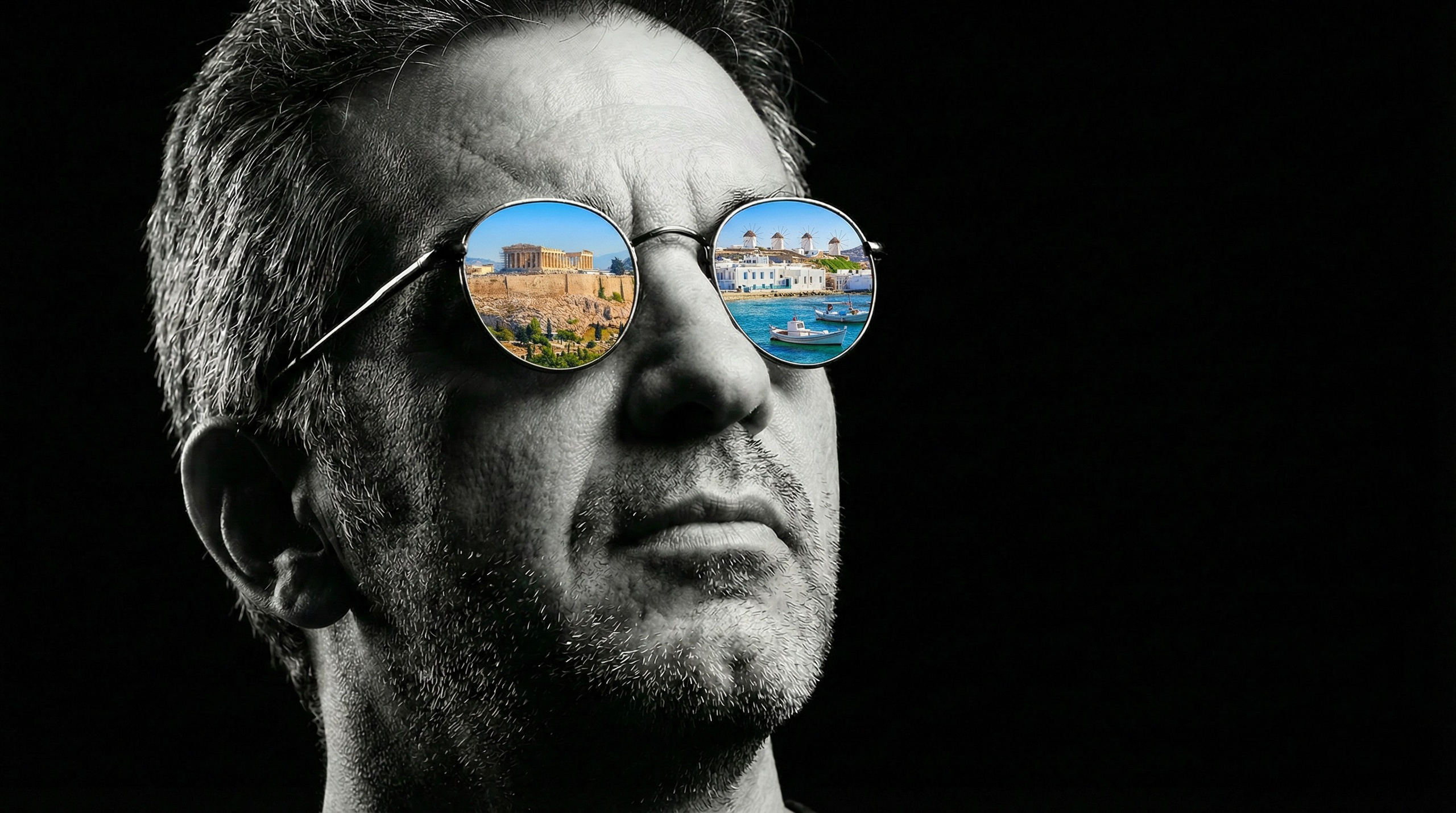Black and white self-portrait of photographer Panagiotis Lymperopoulos wearing round, reflective sunglasses that show Athens and Mykonos reflections.